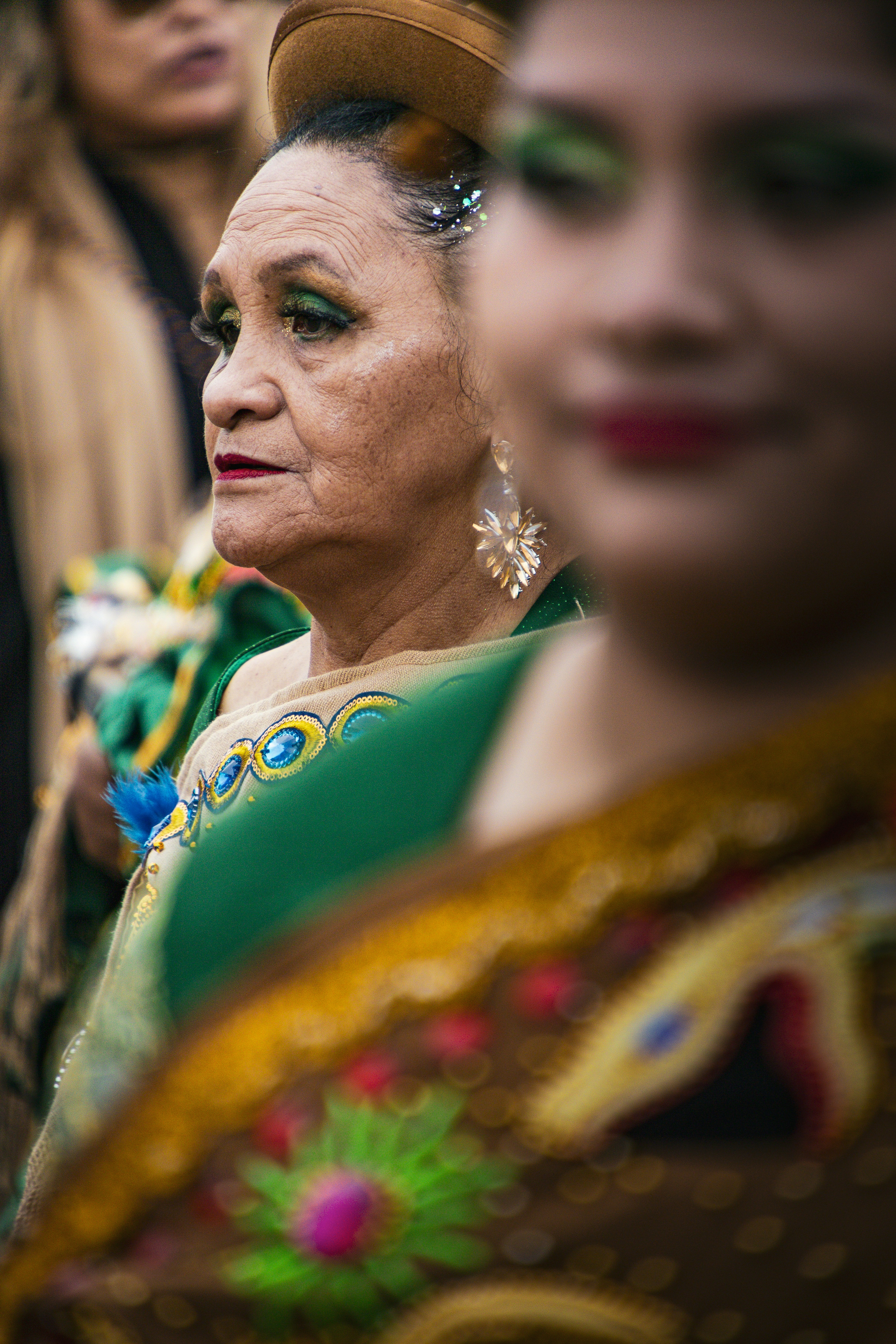 Uma mulher vestindo uma peça verde bordada e um chapéu, com sombra de olhos verde.