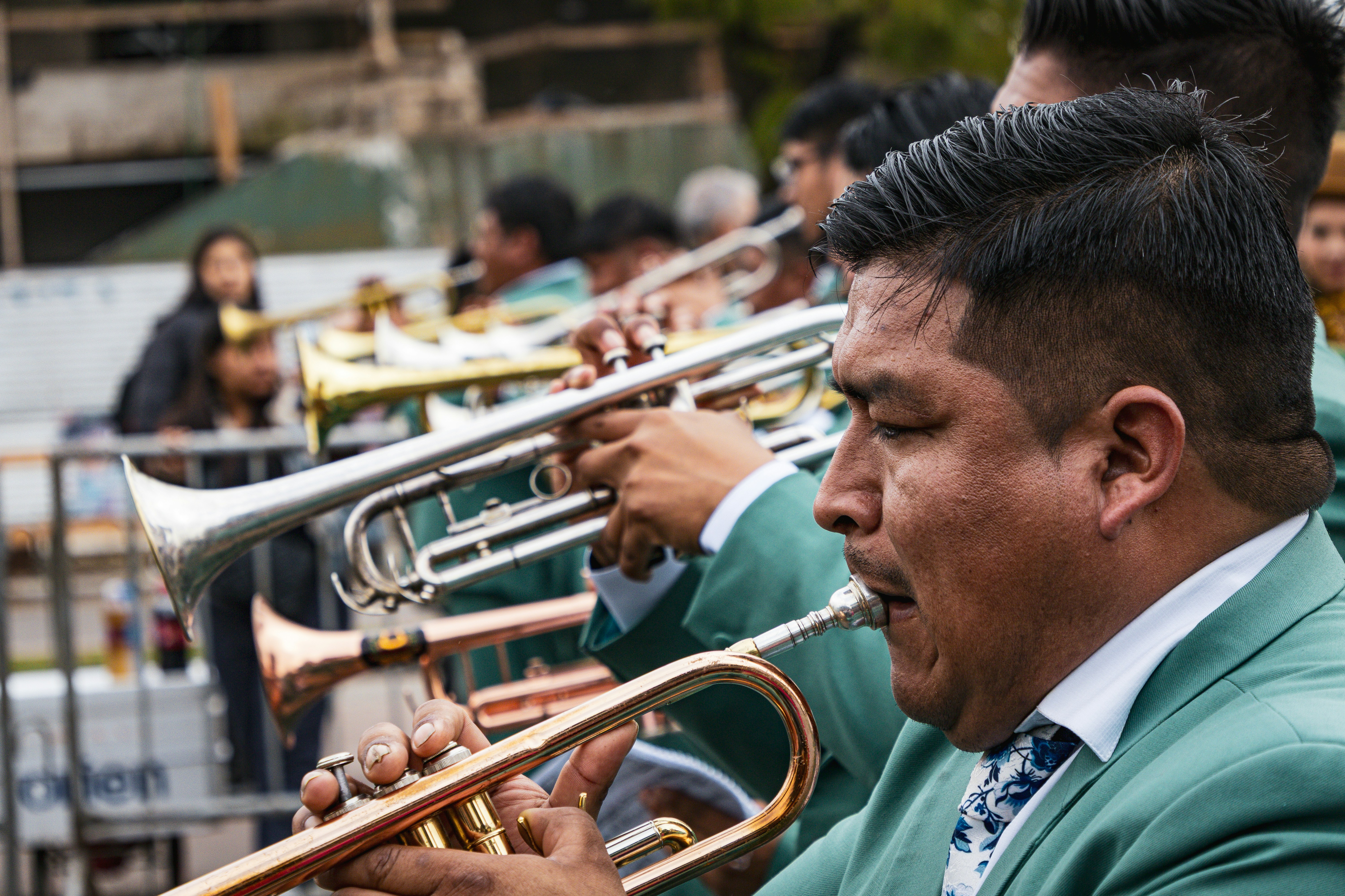 Um grupo de músicos de jaquetas verdes tocando trompetes de metais durante um desfile.
