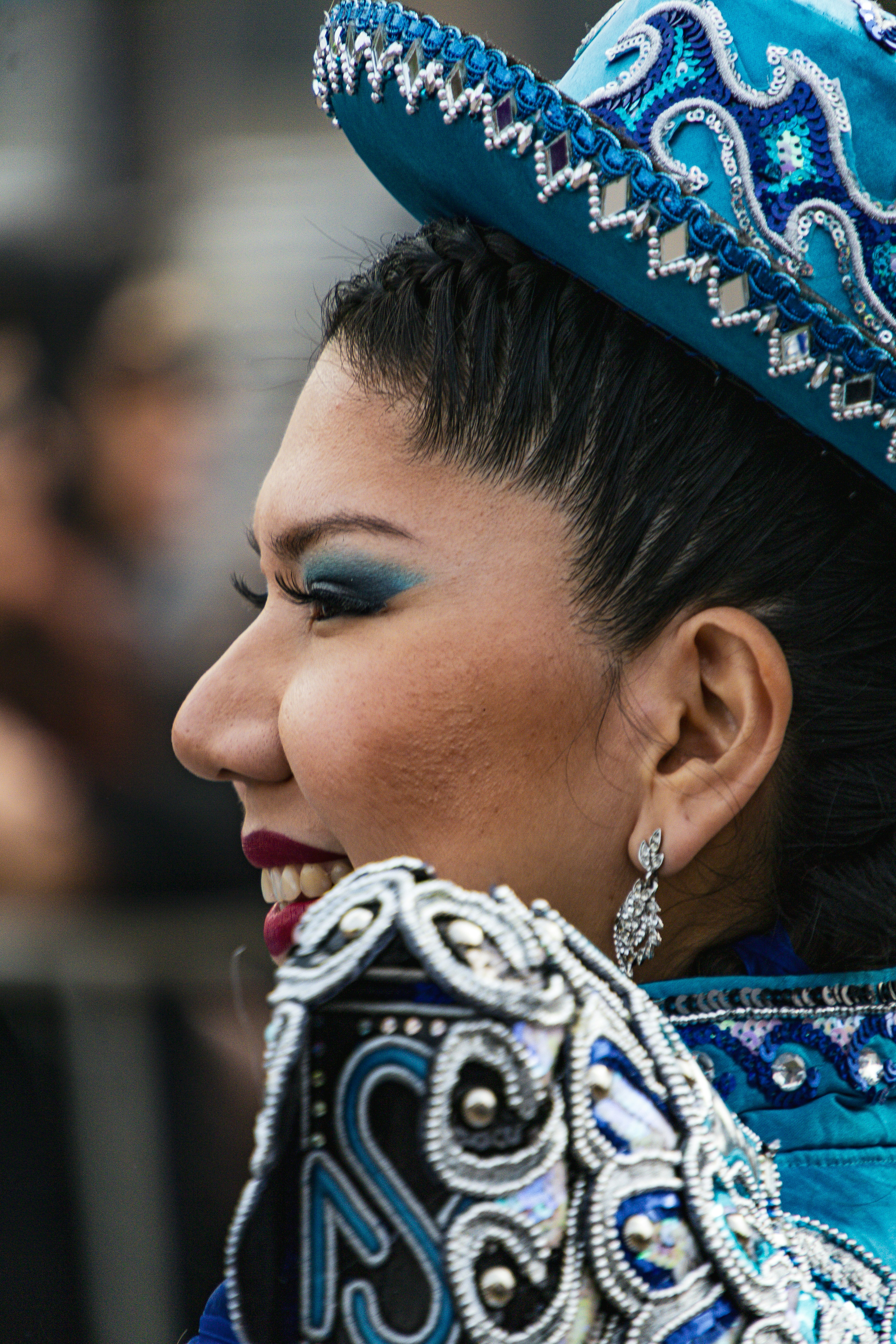 Uma mulher usando um chapéu azul com lantejoulas e um traje ornamentado de perfil.