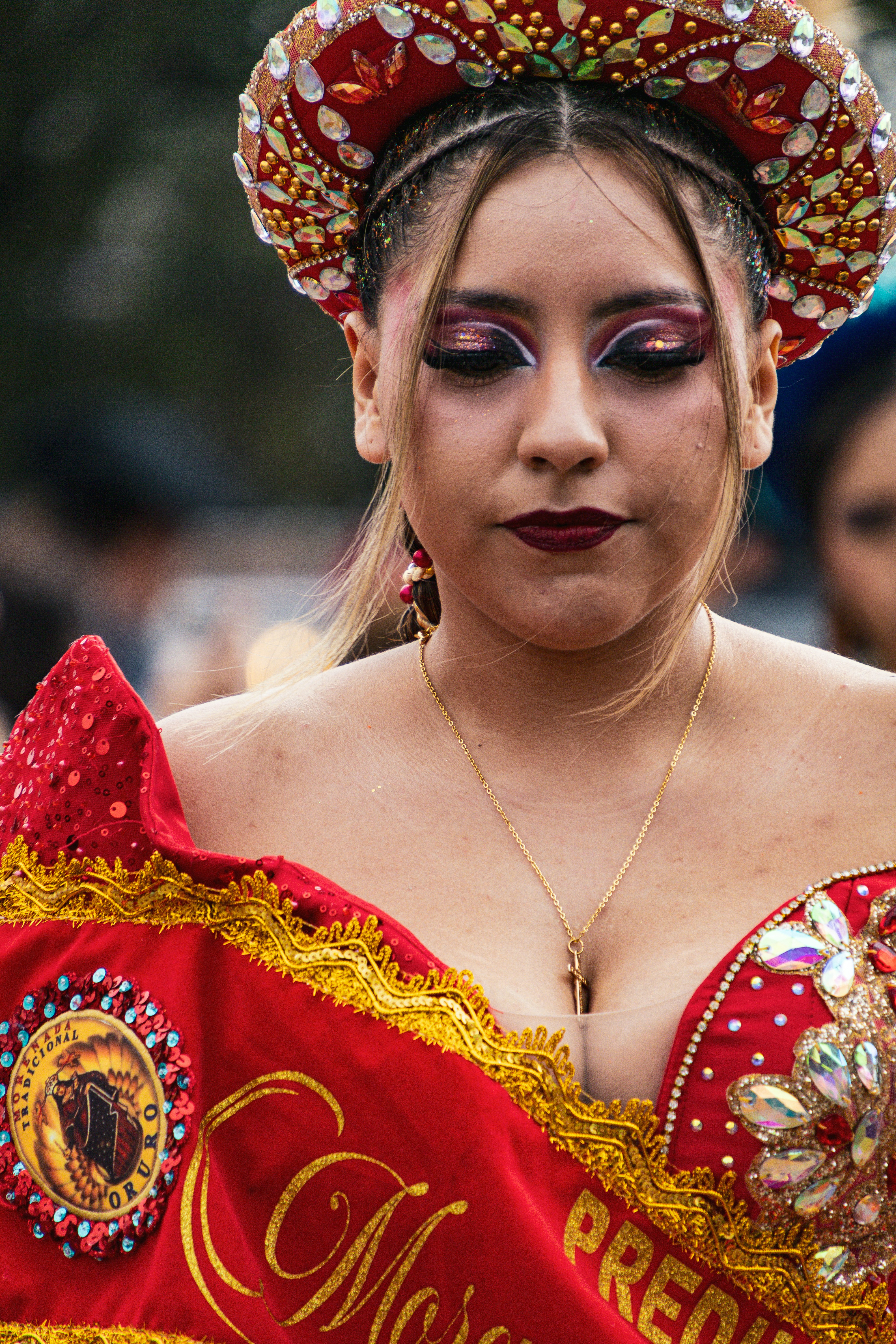 Uma mulher vestindo um traje vermelho de lantejoulas e um adorno de cabeça ornamentado com joias coloridas.