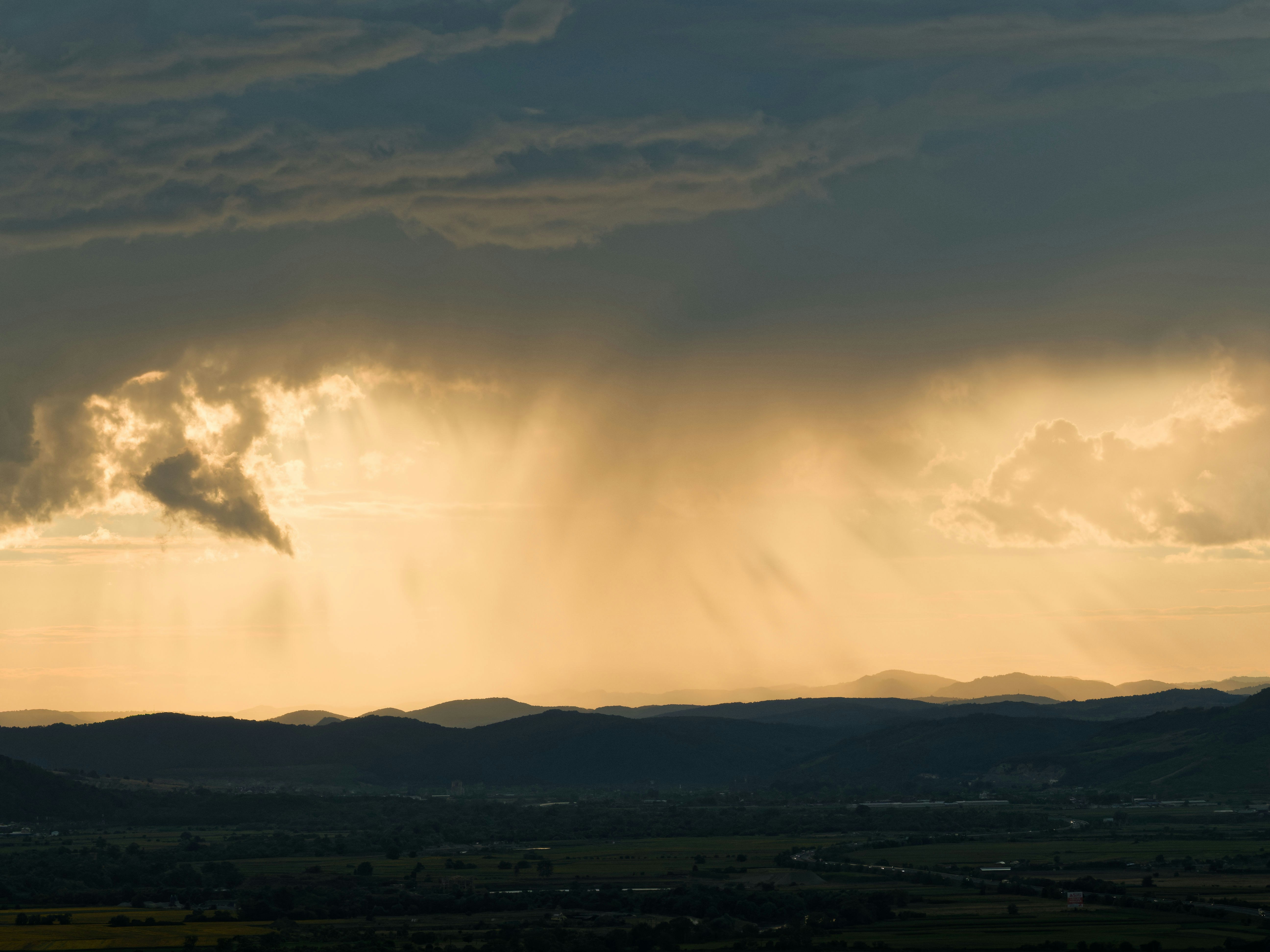 Rain falling from dramatic clouds over distant mountains at sunset.