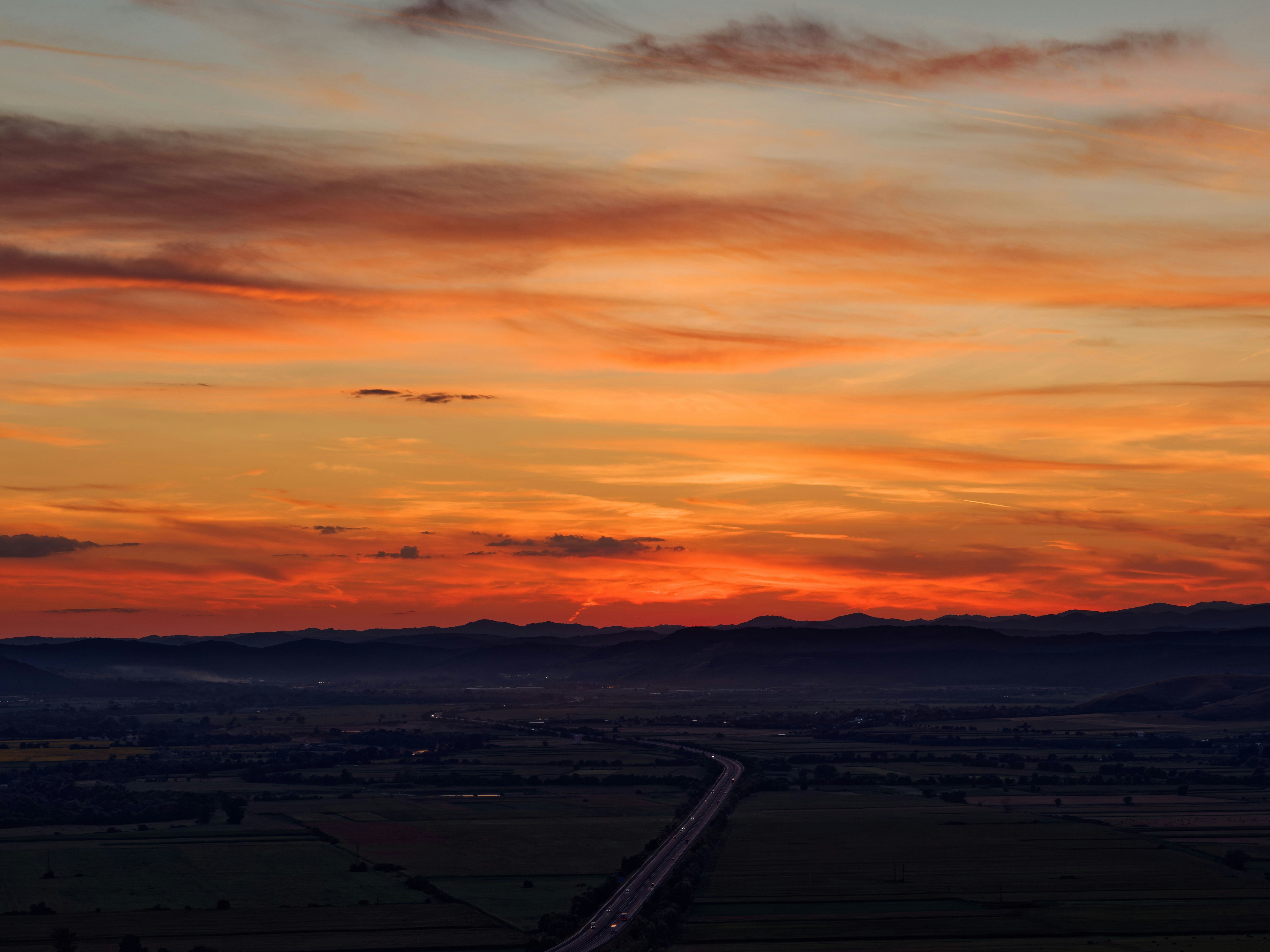 Fiery sunset illuminates dark valley and a winding road.