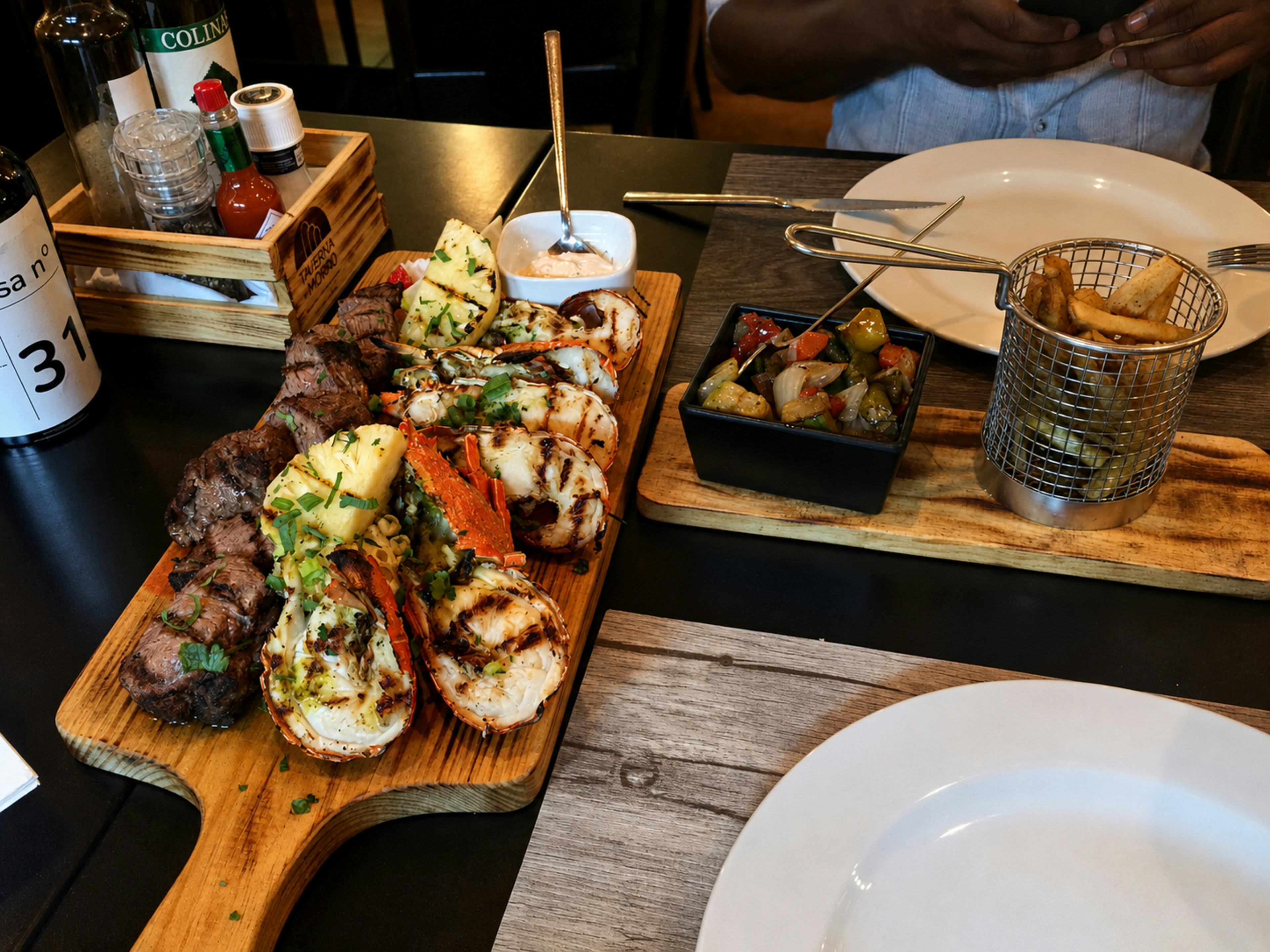 Grilled steak, lobster, and pineapple on a wooden board with fries and vegetables