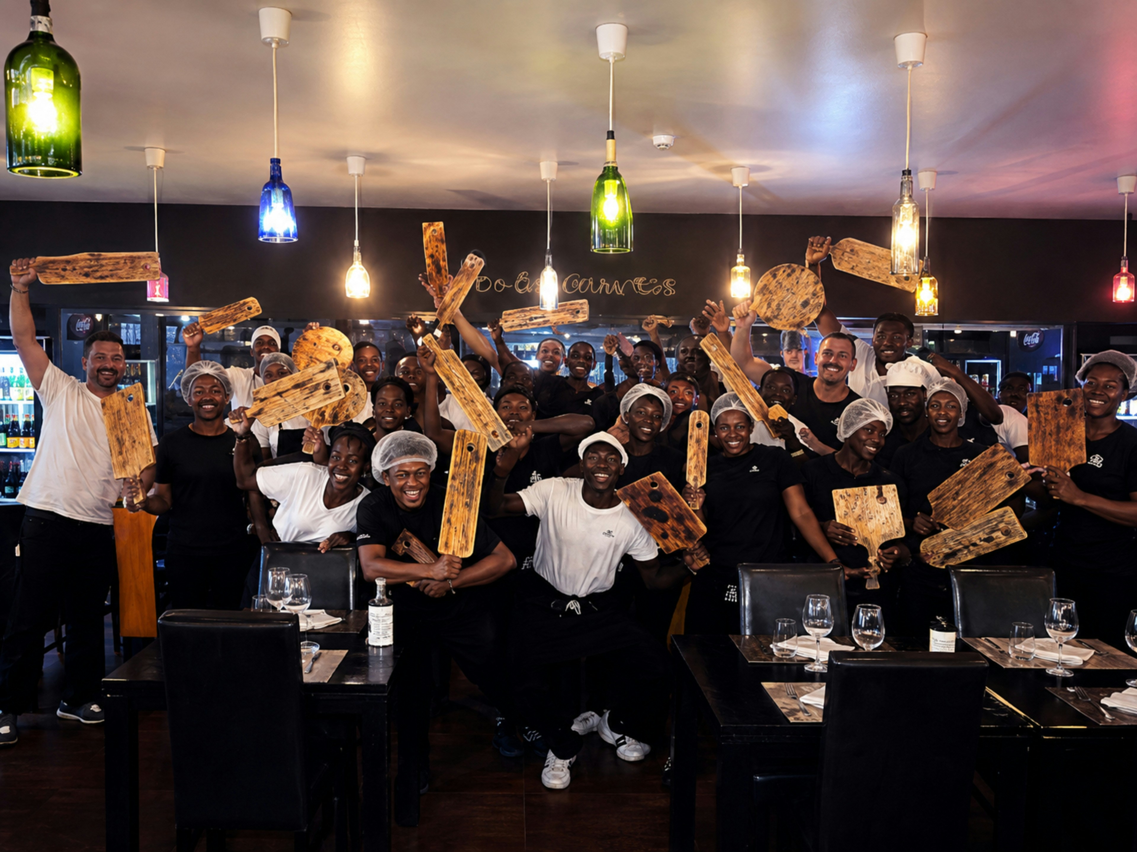 A large group of restaurant staff holding wooden serving boards in a dining room.