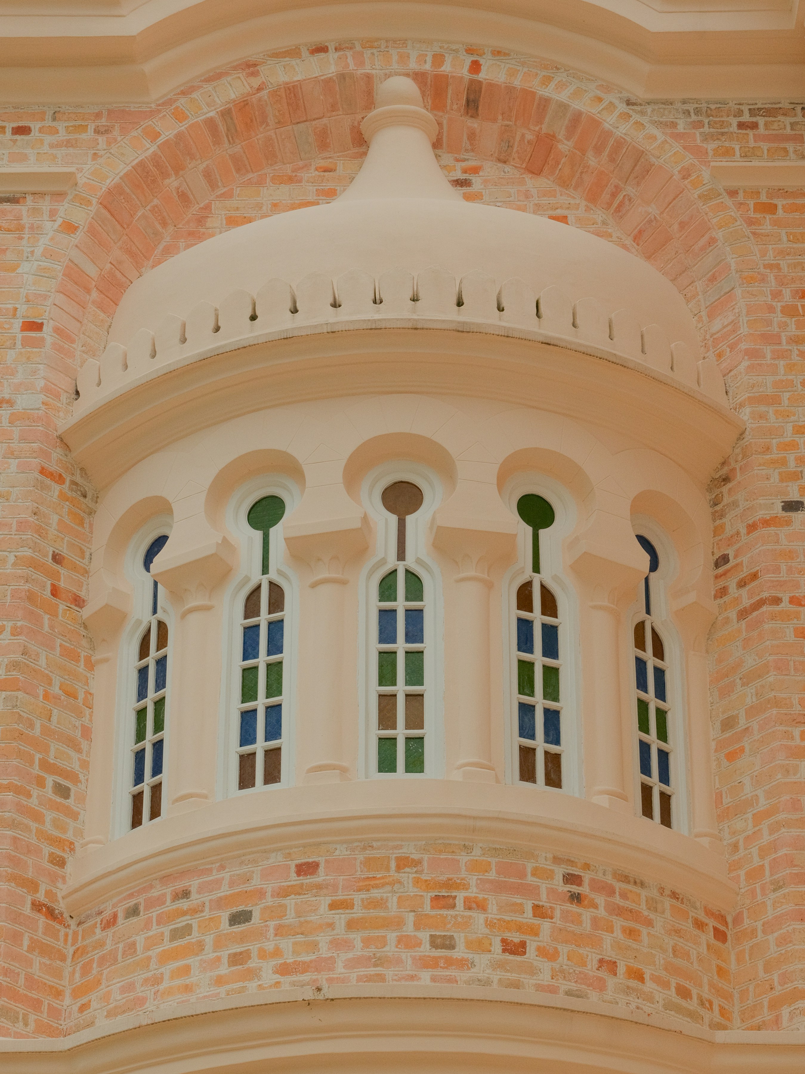 Ornate window with colorful stained glass on a brick building.