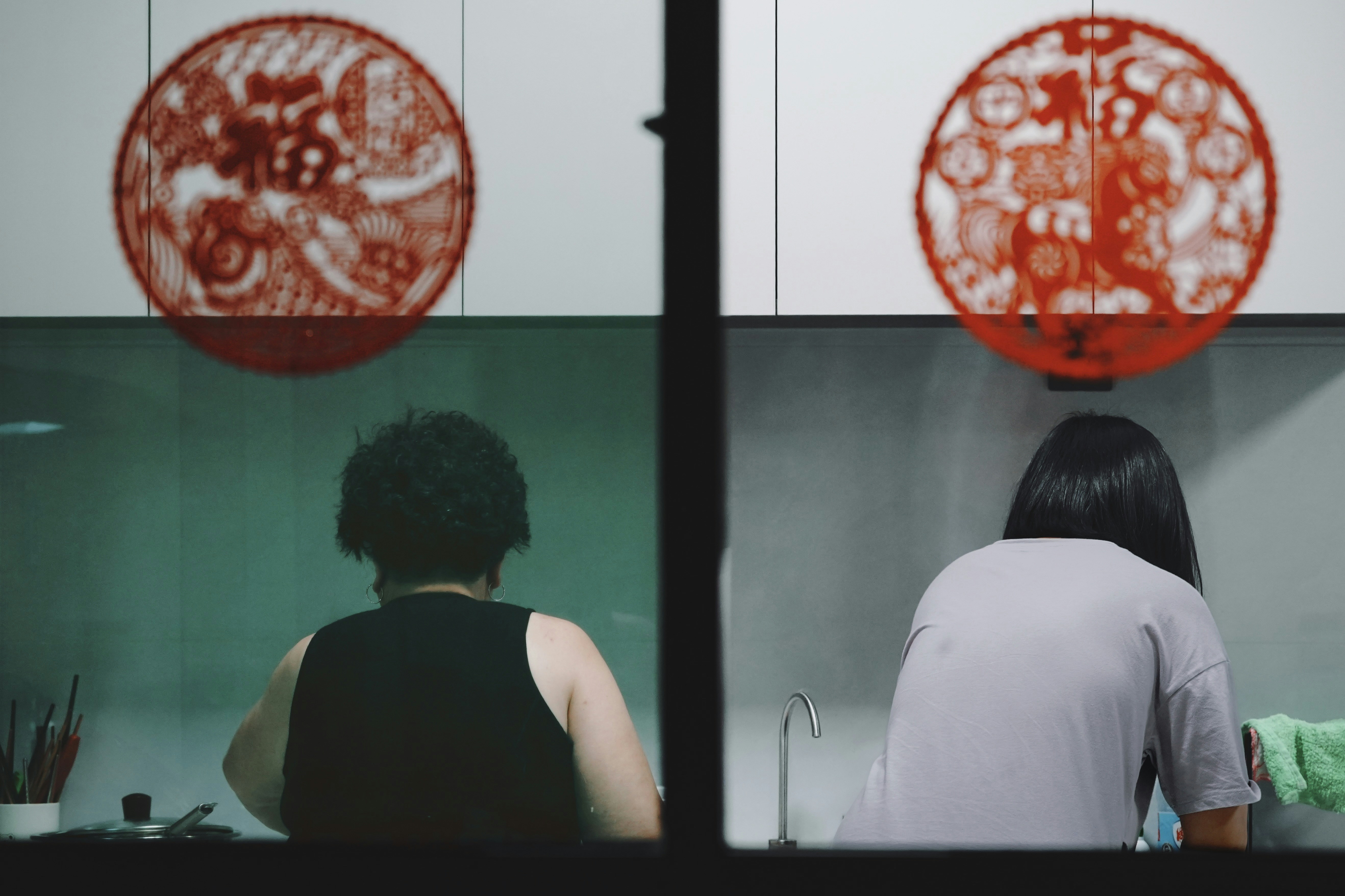 Deux personnes travaillant dans une cuisine avec des coupures de papier rouge.