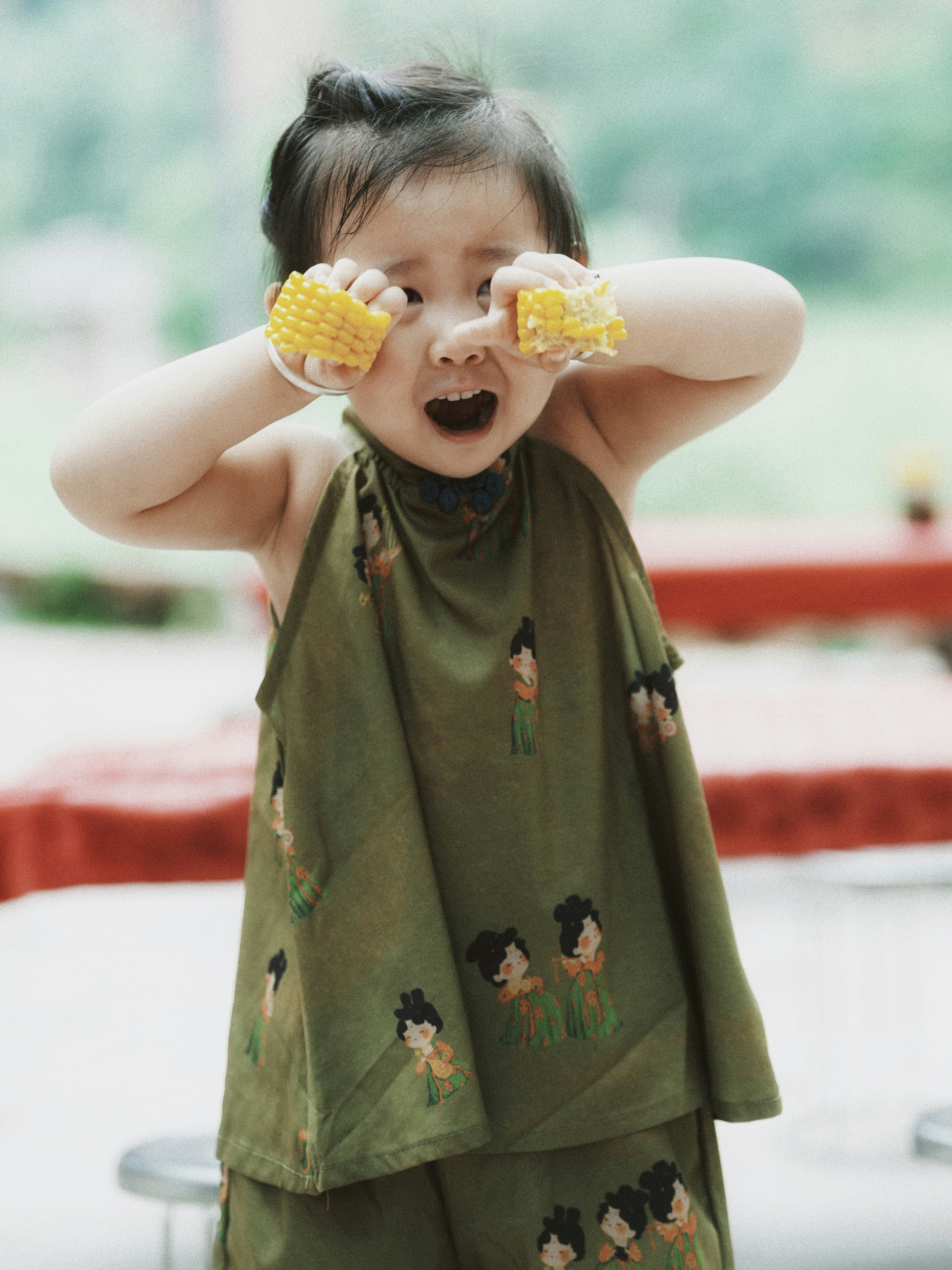 A child playfully holds corn cobs over their eyes