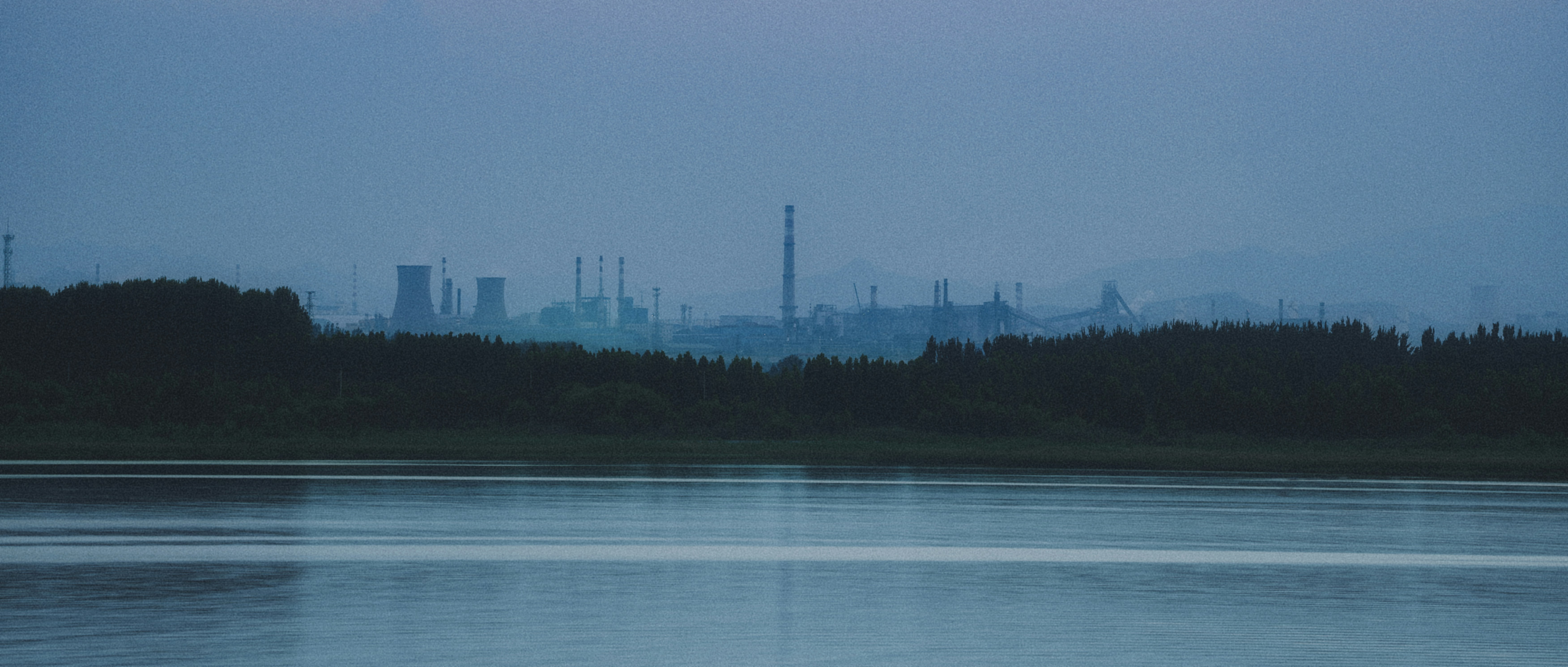 Hazy industrial complex across a calm lake