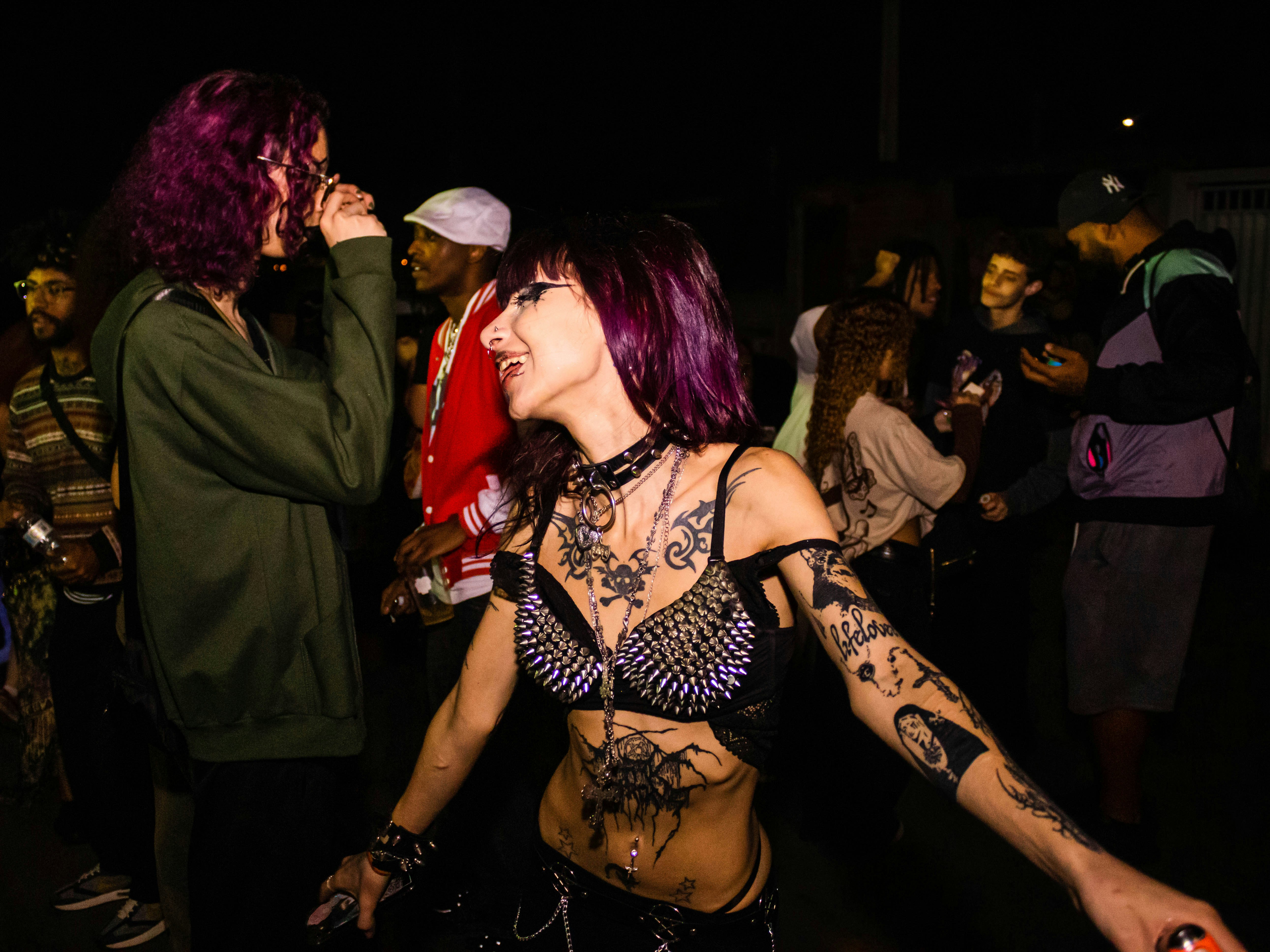 Tattooed woman with purple hair dancing among people at night