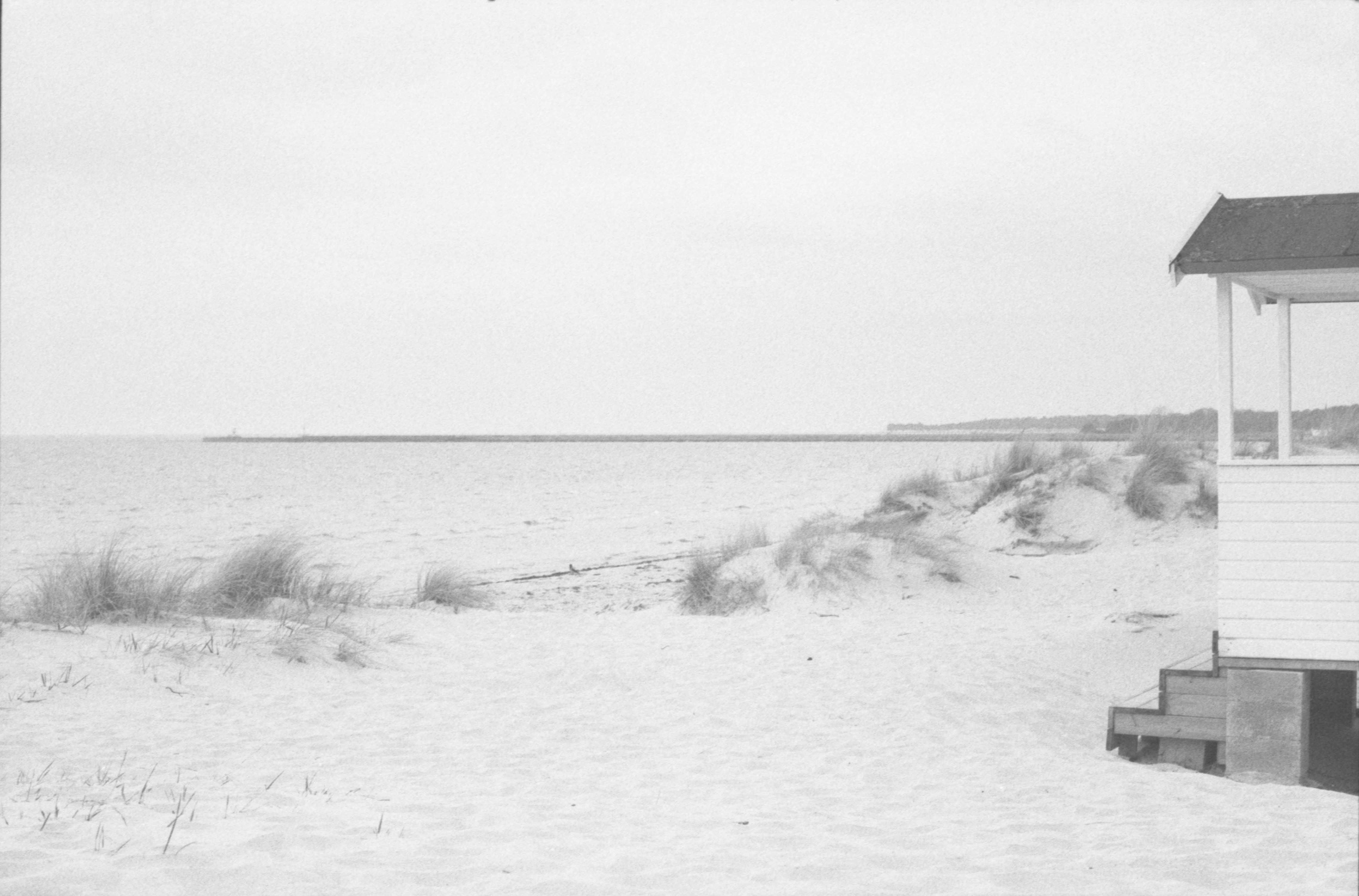 Sandy beach with dunes and a building by the water.