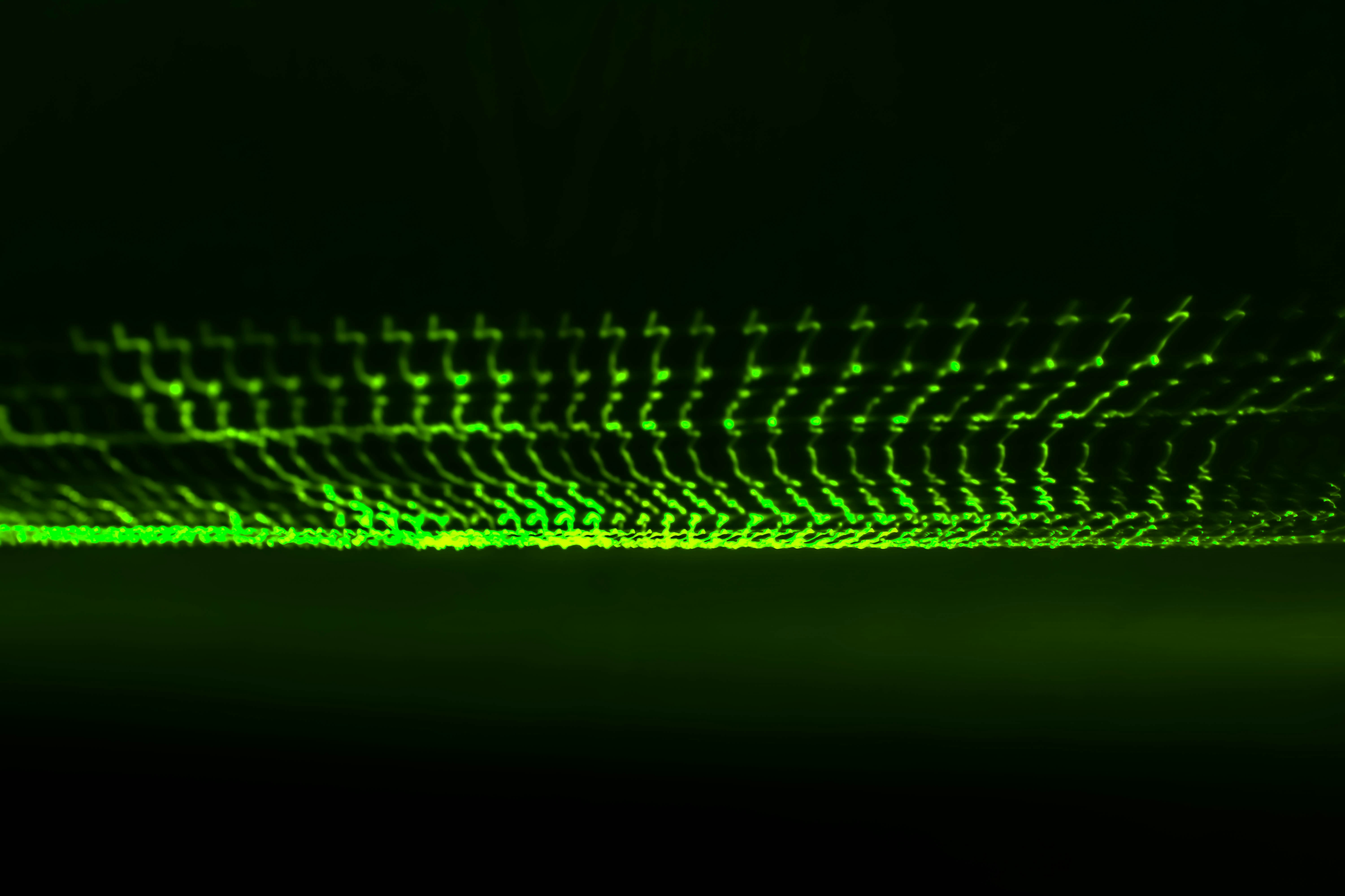Green glowing particles forming a horizontal pattern on dark background.