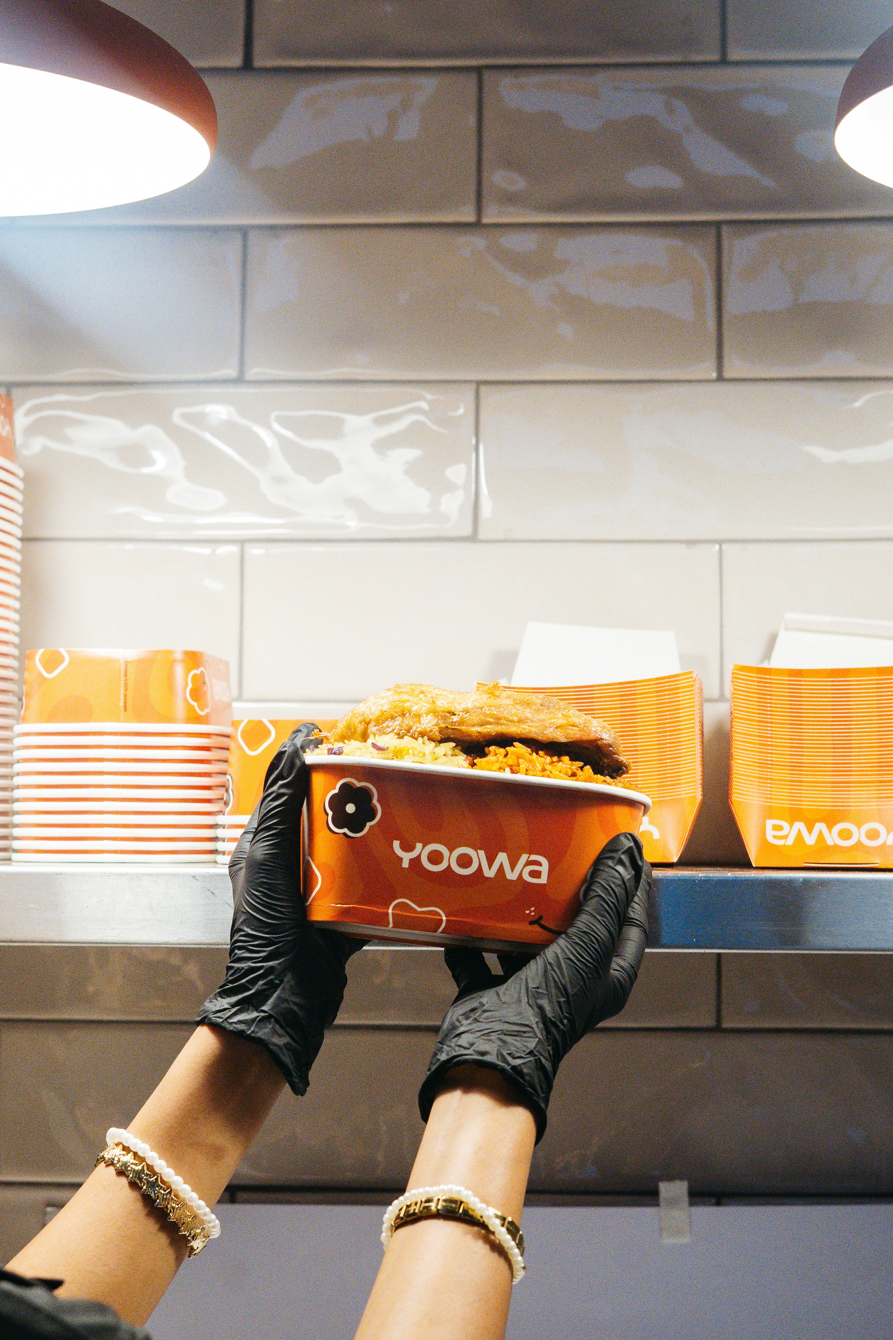 Hands in black gloves holding a yoowa food container.