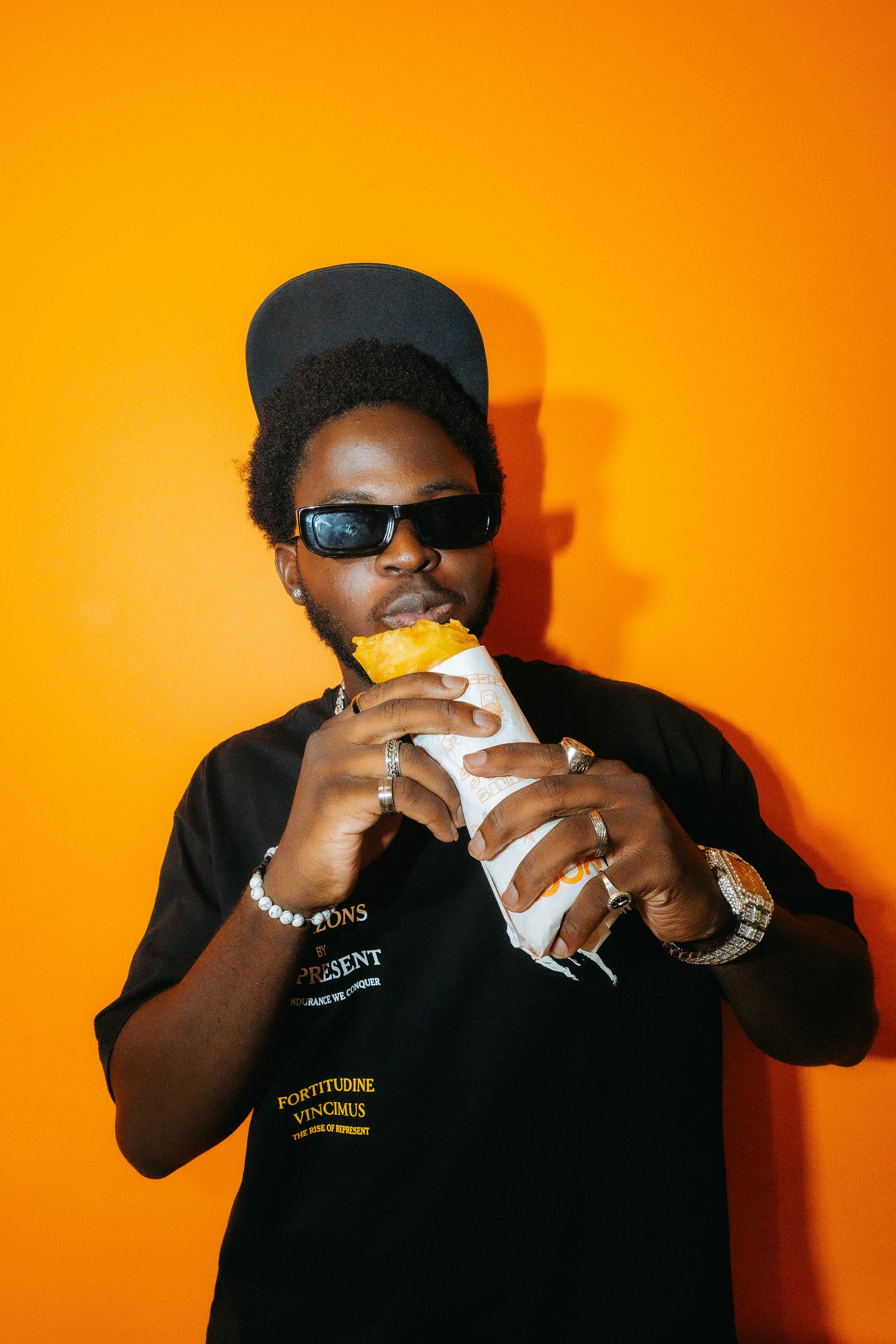 Stylish man eating a wrap against a vibrant orange background.
