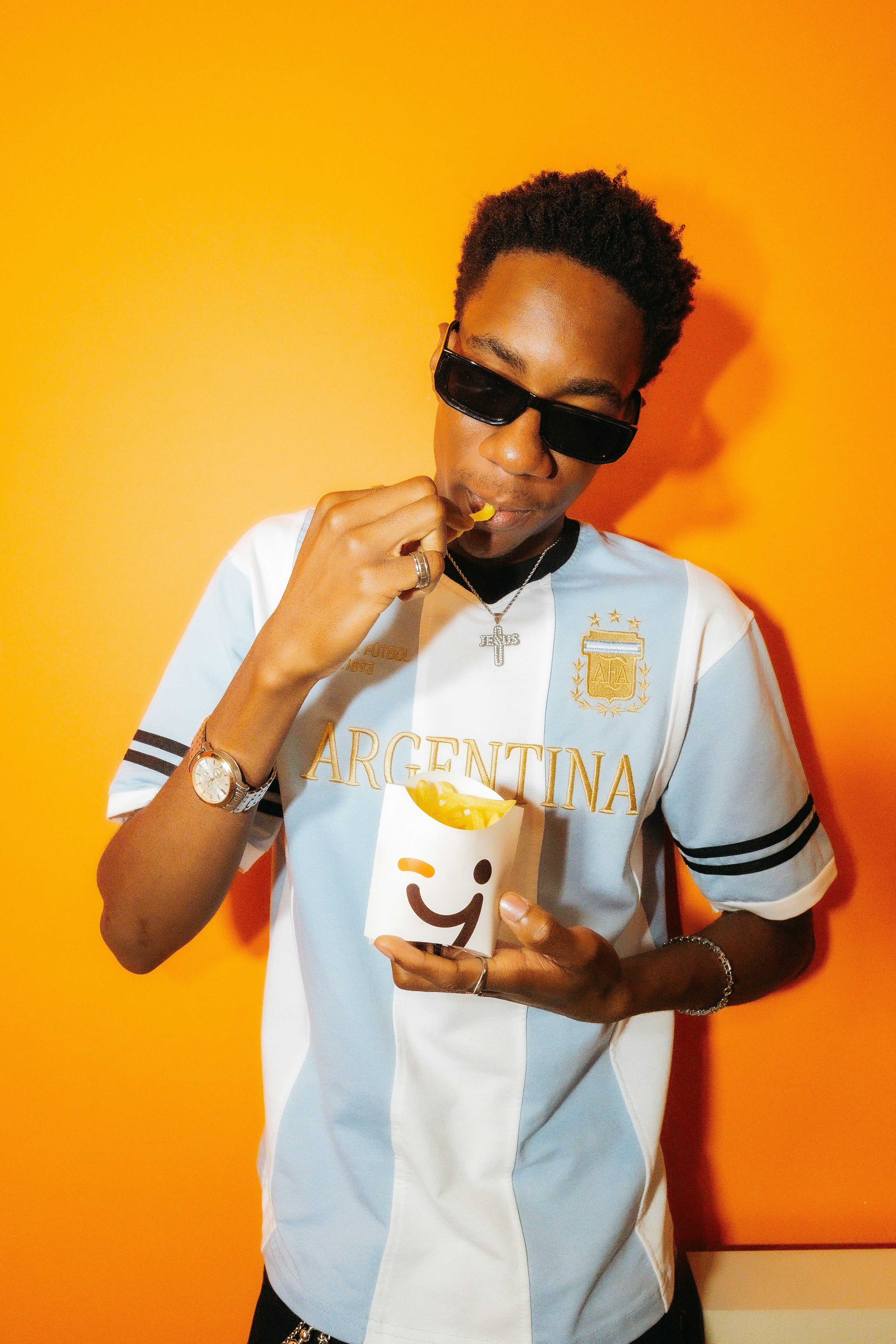 A young man eating fries against an orange background.