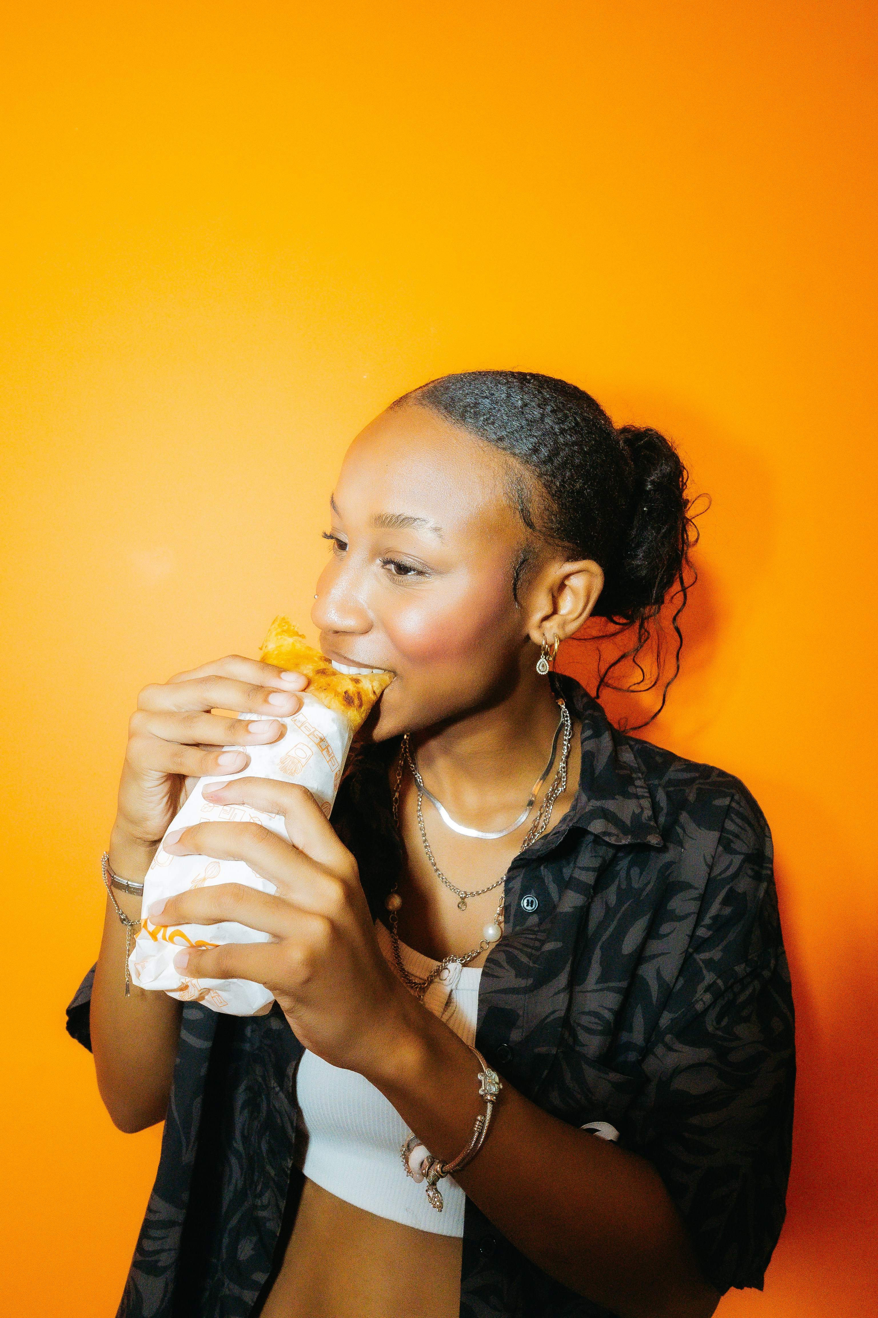 Happy woman eating a burrito against a bright orange wall.