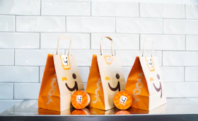 Three smiling paper bags and lion-branded items on white tiles.