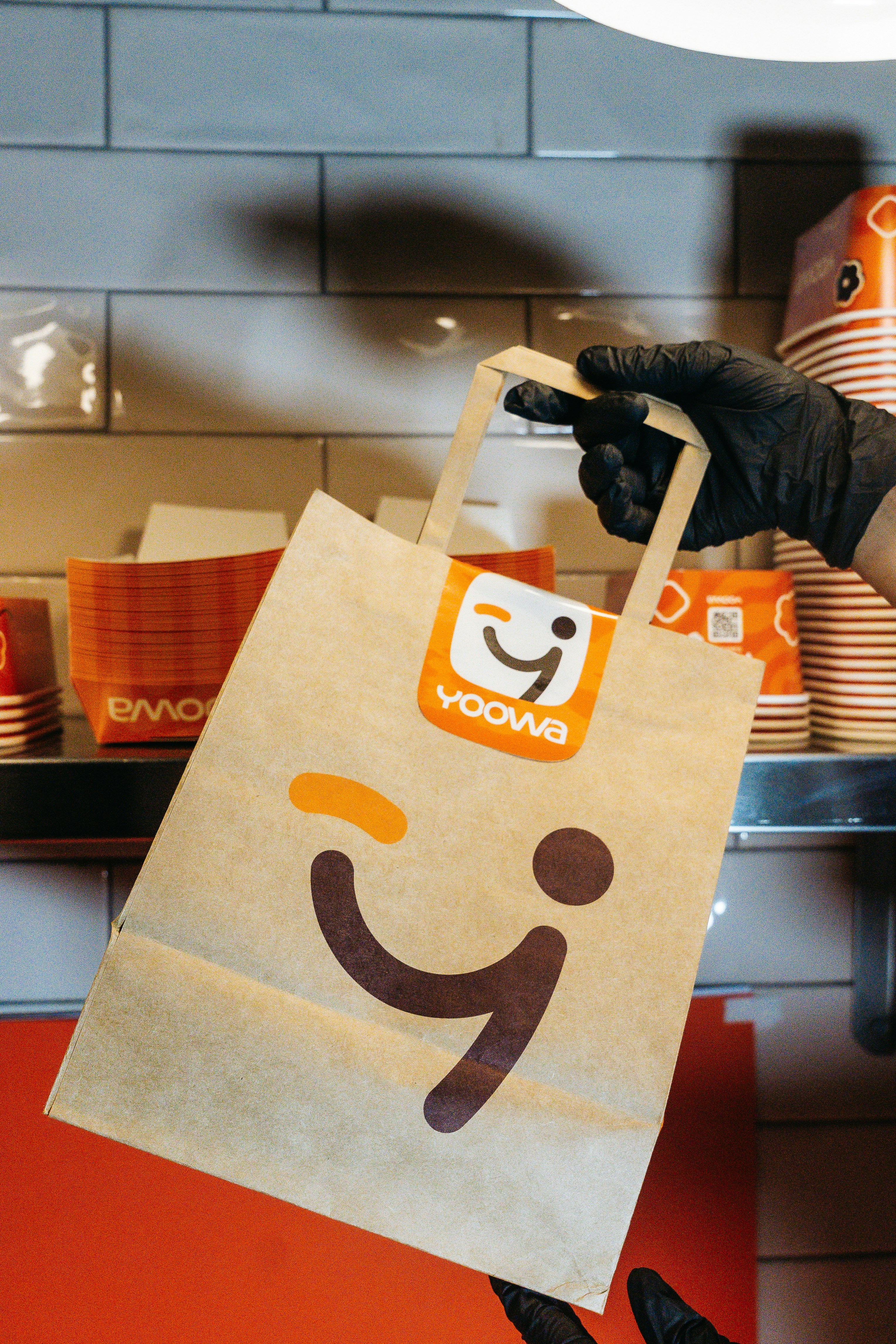 A gloved hand holds a yoowa branded paper bag.