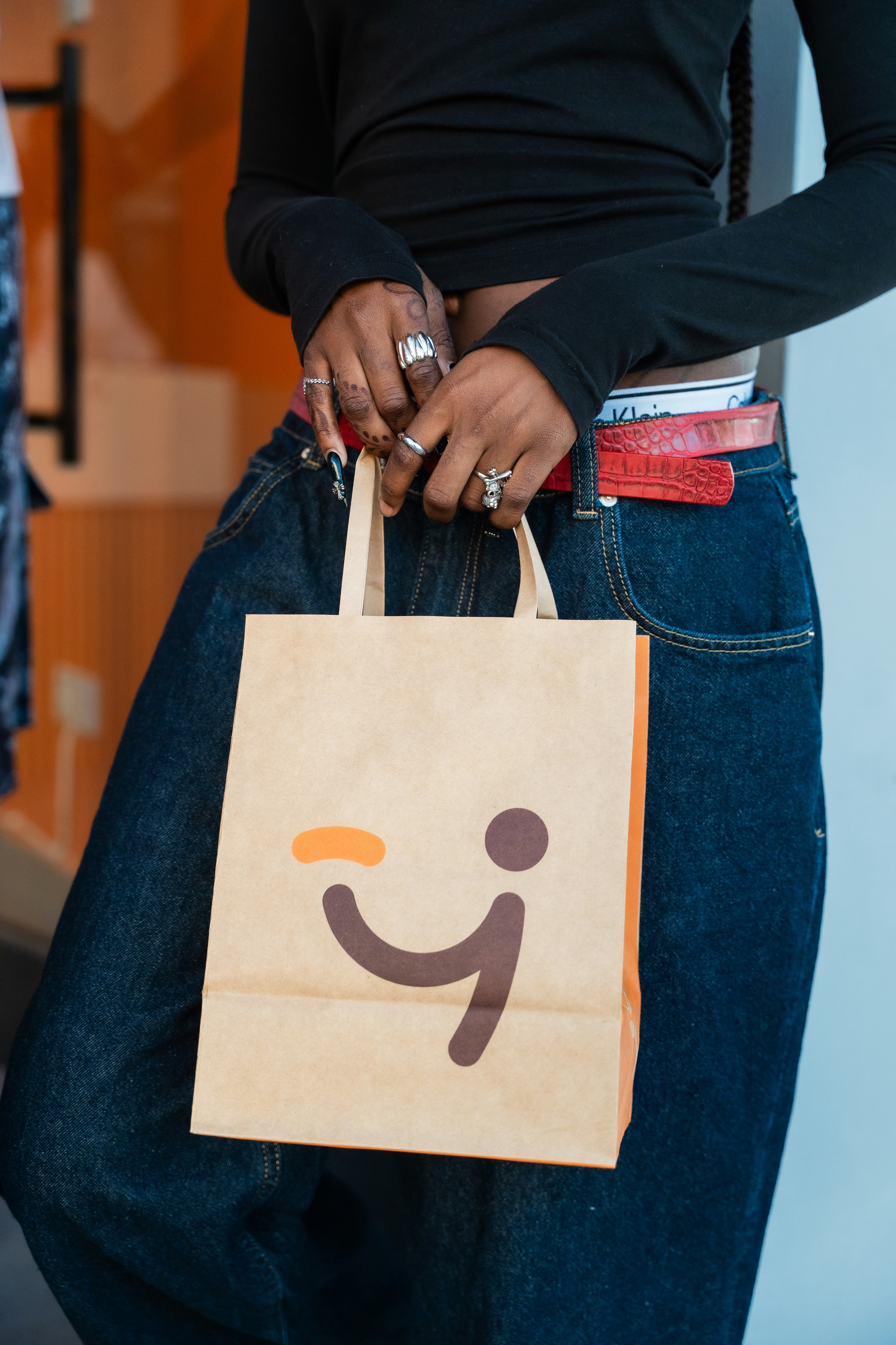 Person holding a brown paper bag featuring a winking face.