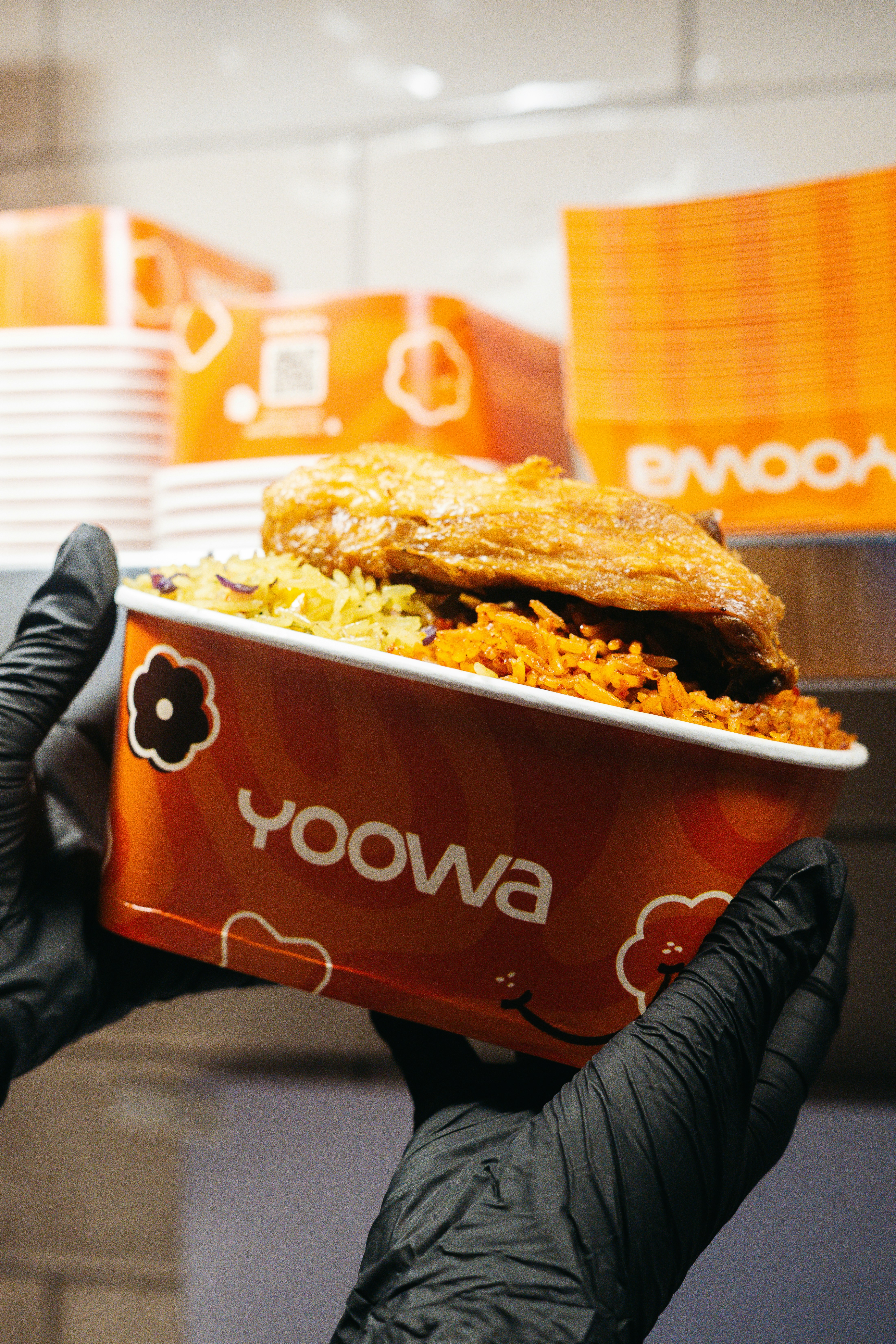 Hands holding an orange bowl of rice and fried chicken.