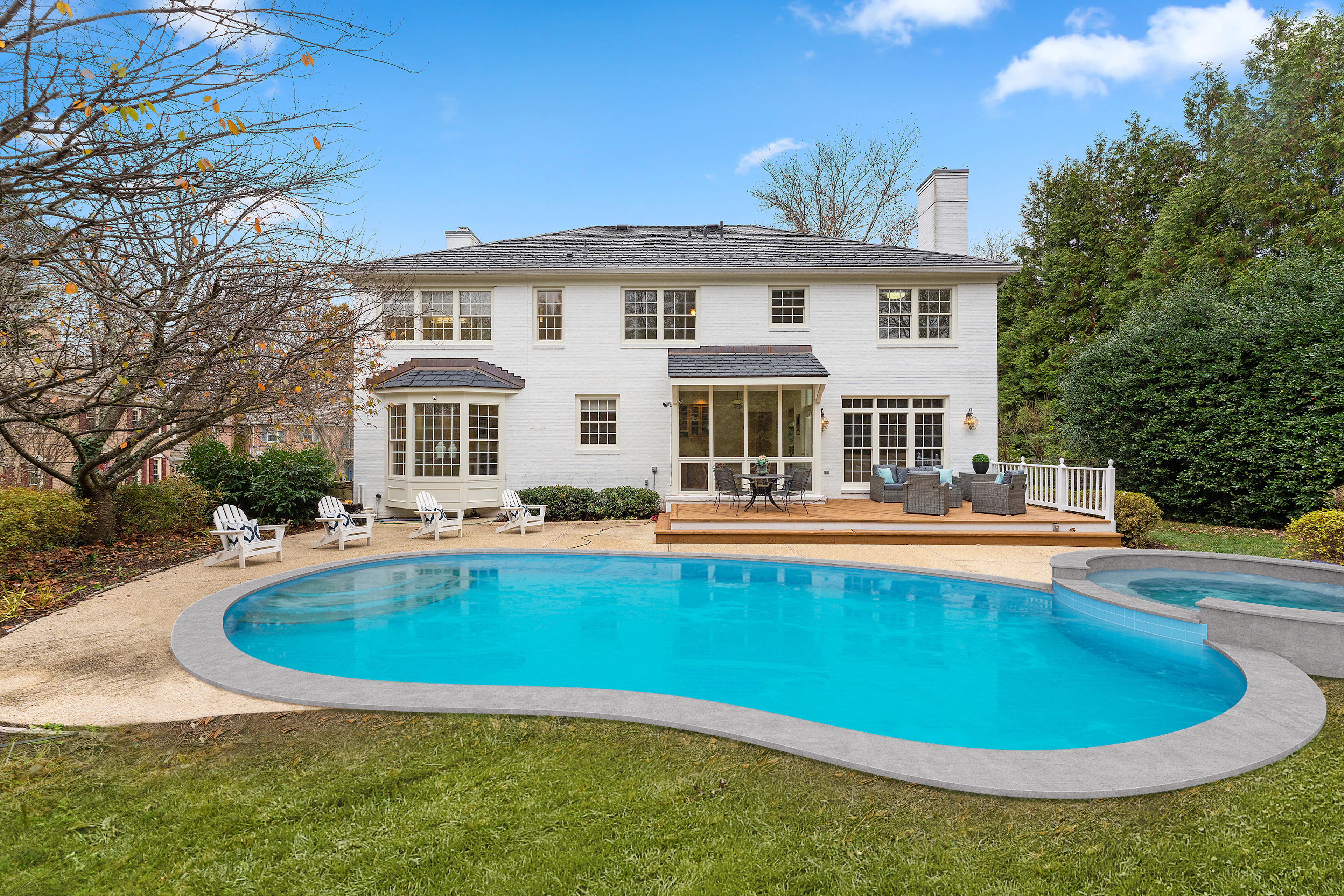 Classic freeform pool with a stone deck behind a traditional two-story home