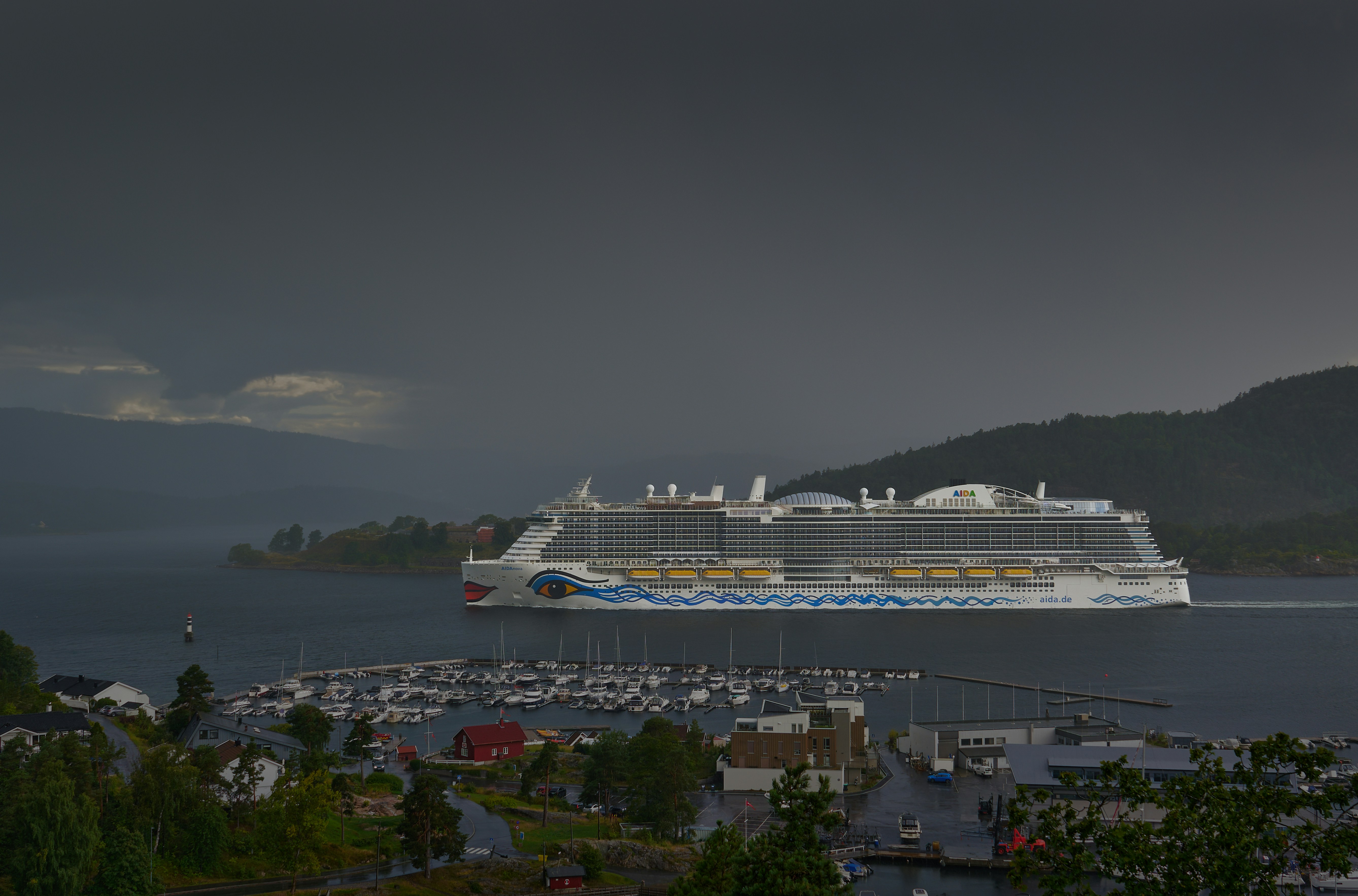 Cruise ship passing a harbor town with mountains.