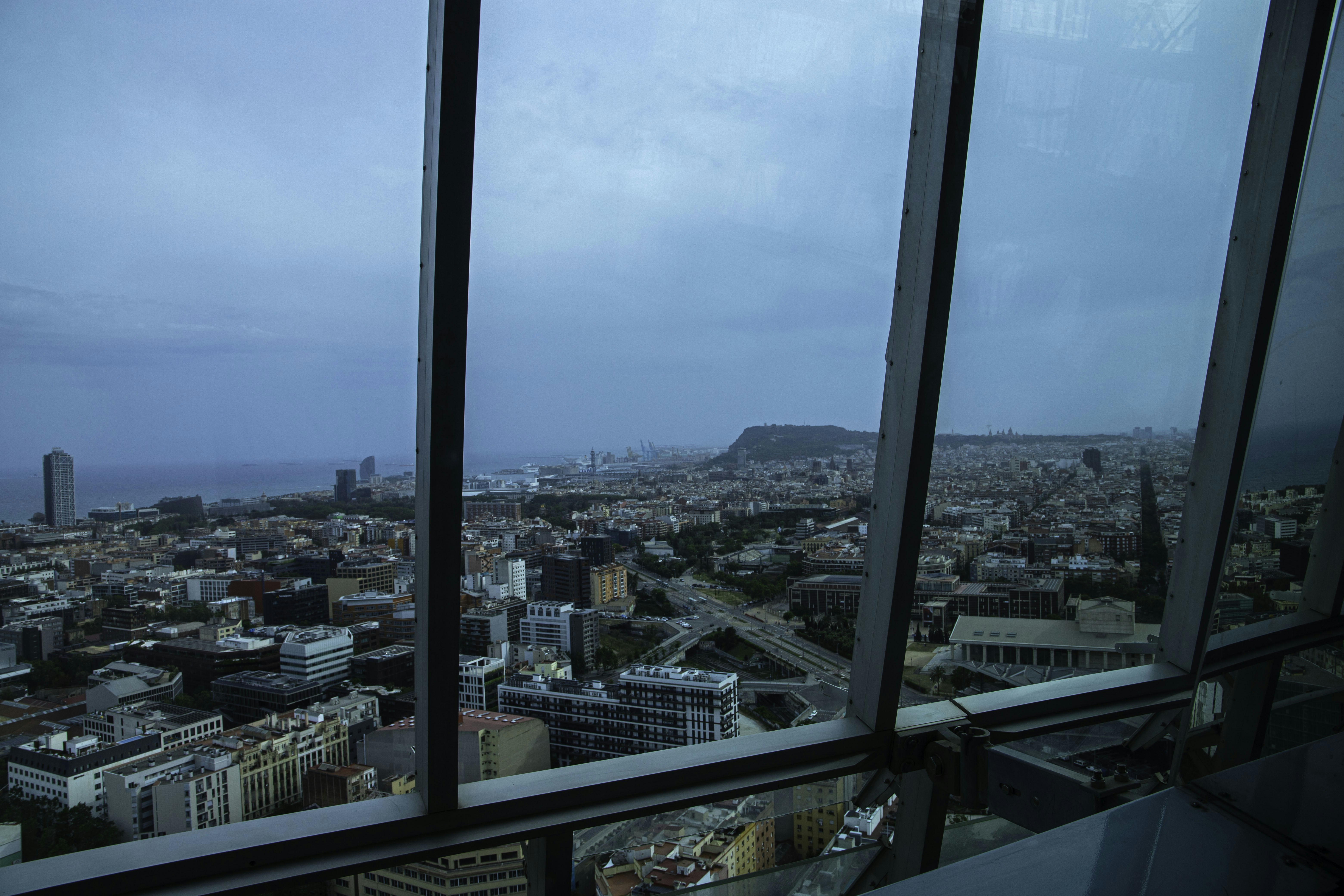 Paysage urbain depuis une fenêtre haute donnant sur la ville, la mer et la montagne.