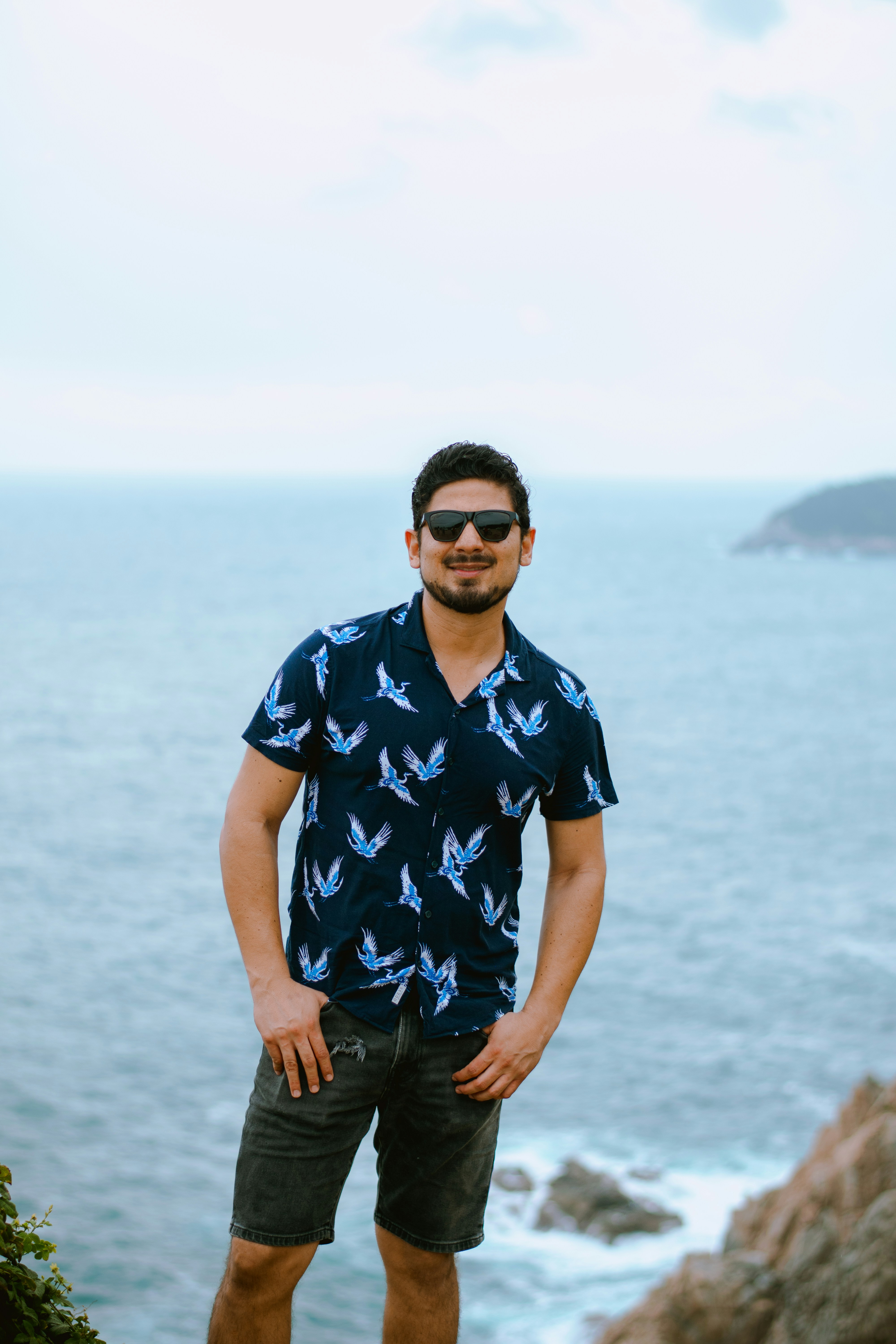 Der lächelnde Mann mit Sonnenbrille steht am weiten blauen Ozean.
