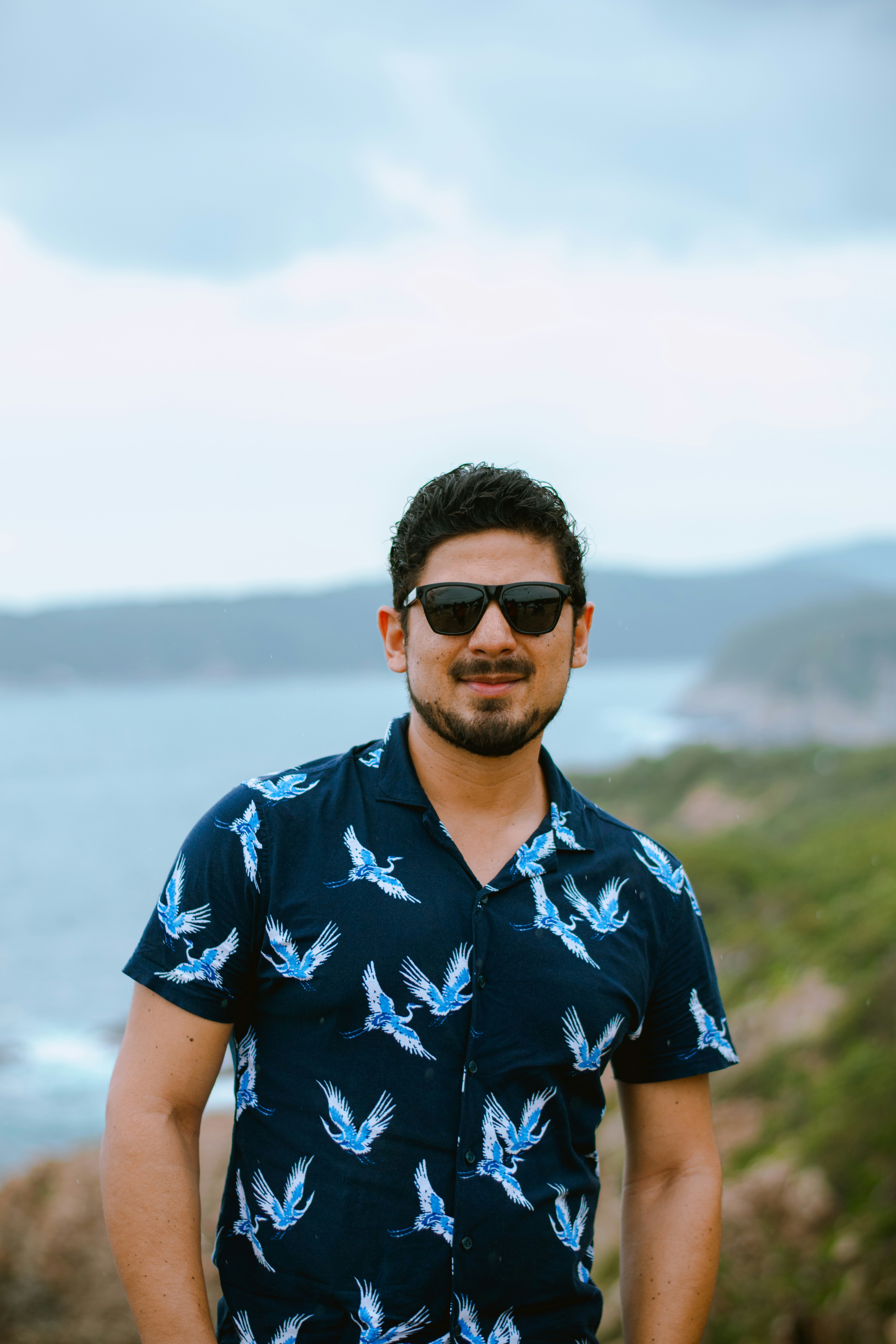 Mann mit Sonnenbrille und gemustertem Hemd am Meer.