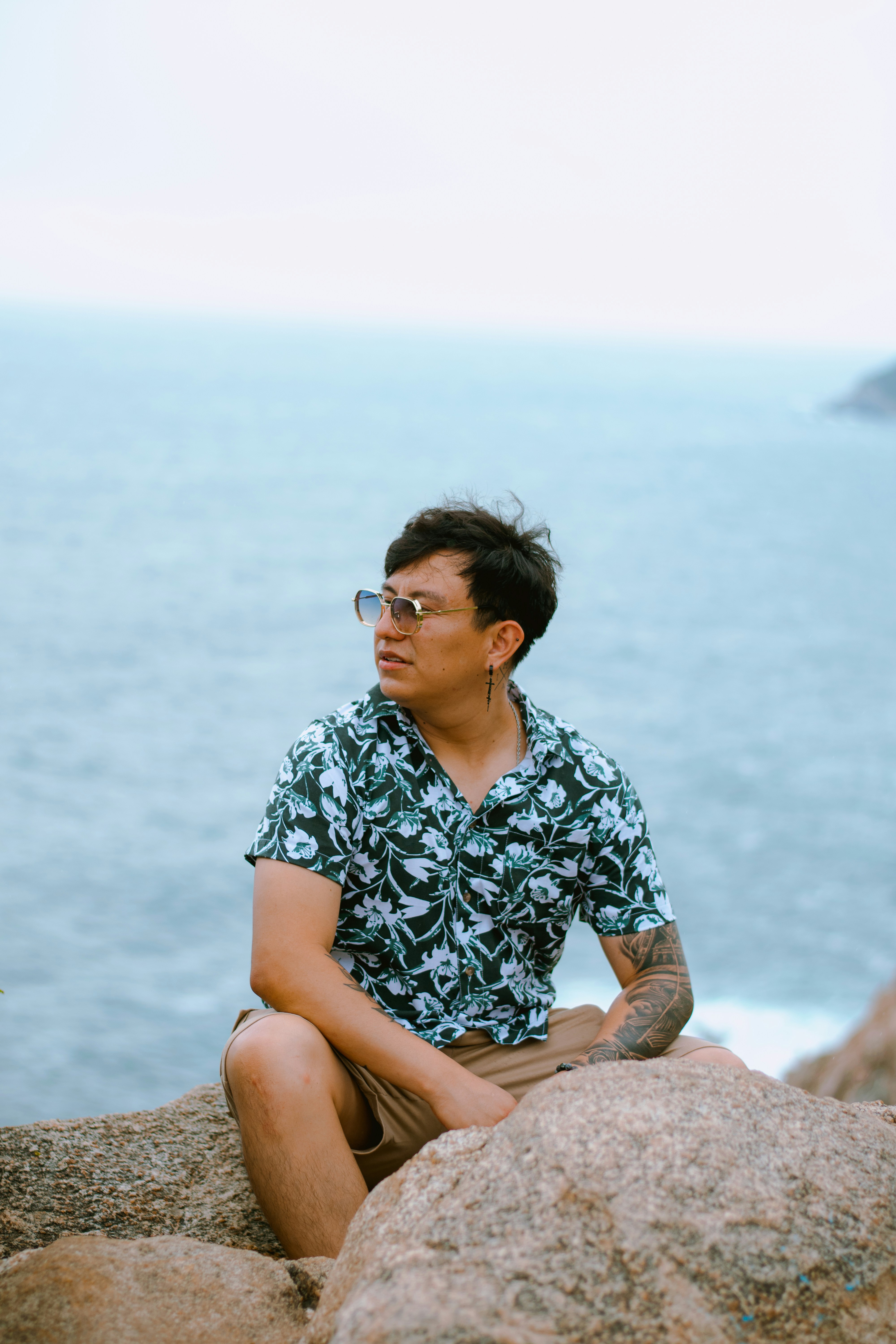 Ein Mann im geblümten Hemd und Sonnenbrille sitzt am Meer.