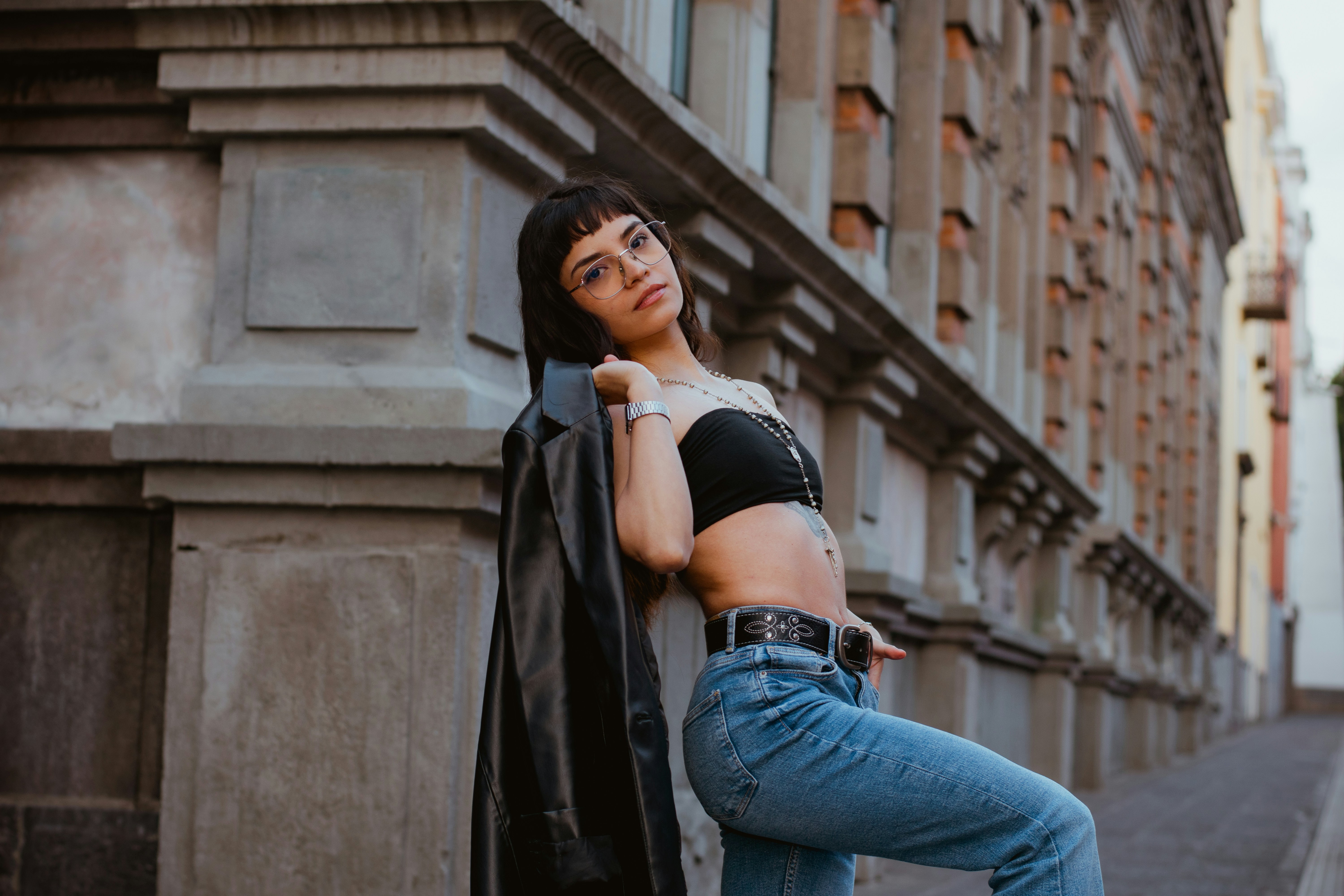 Woman in black crop top and jeans poses by building