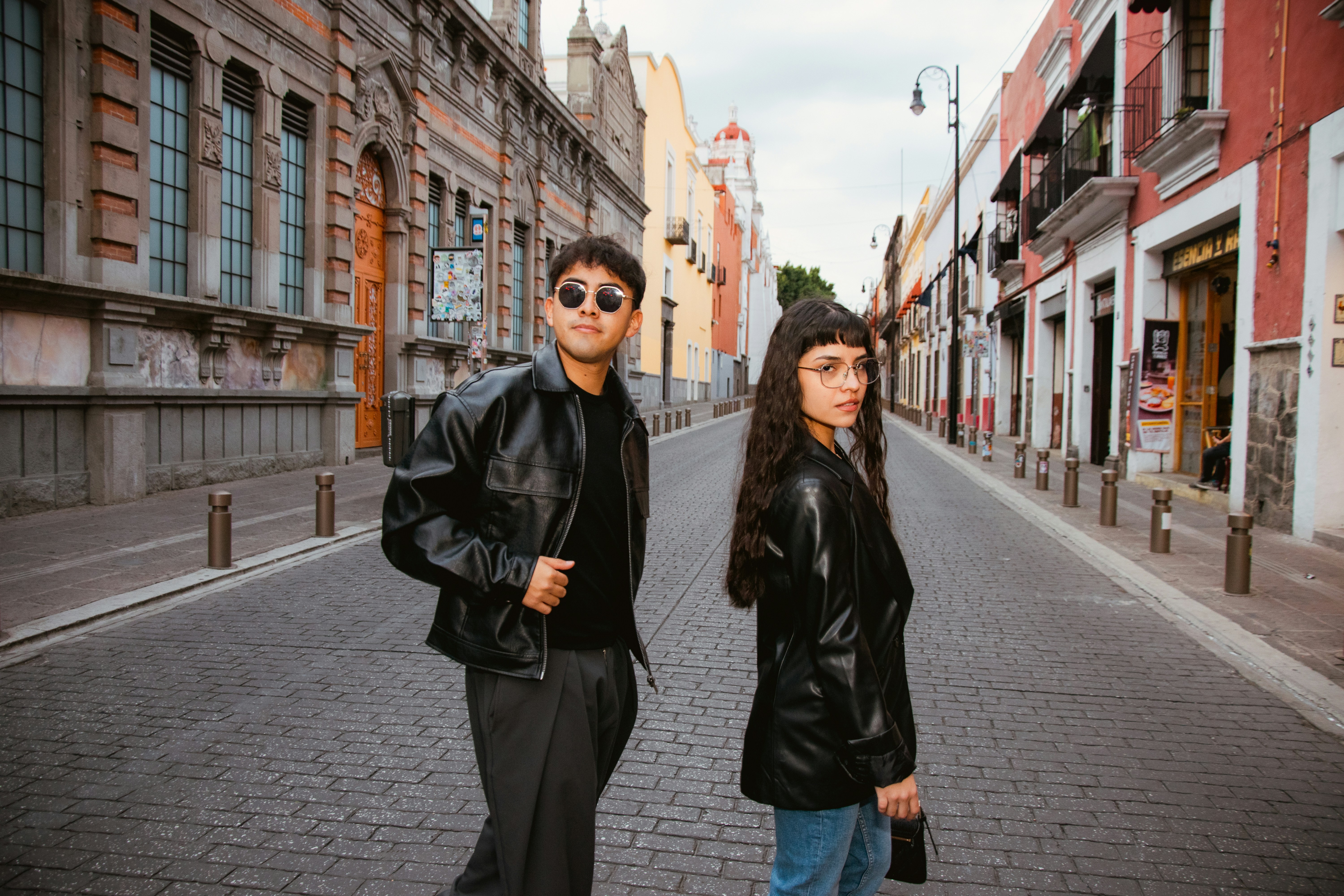 Two people in black jackets stand on a cobblestone street