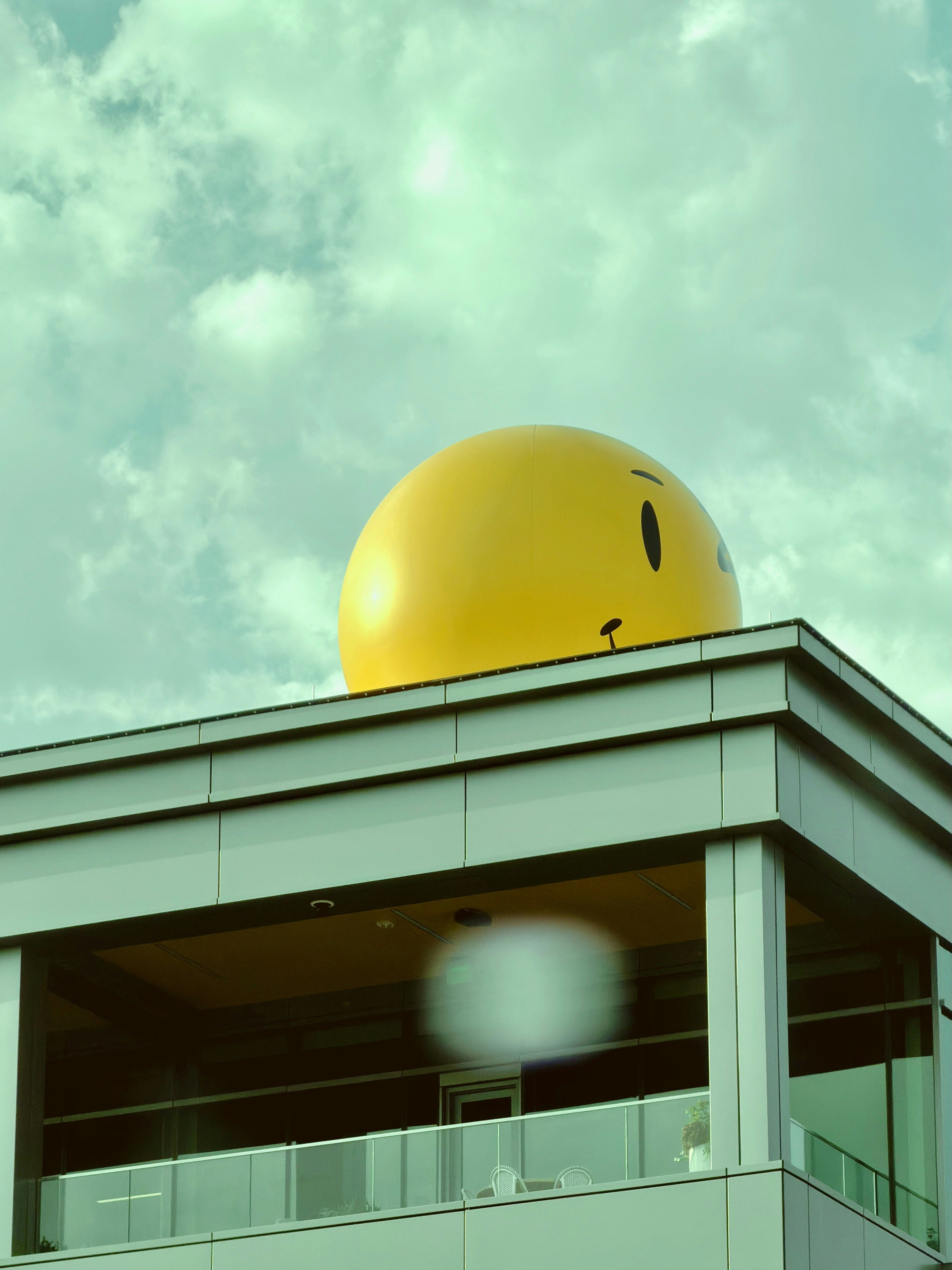 Large yellow smiley face sphere on a modern building rooftop