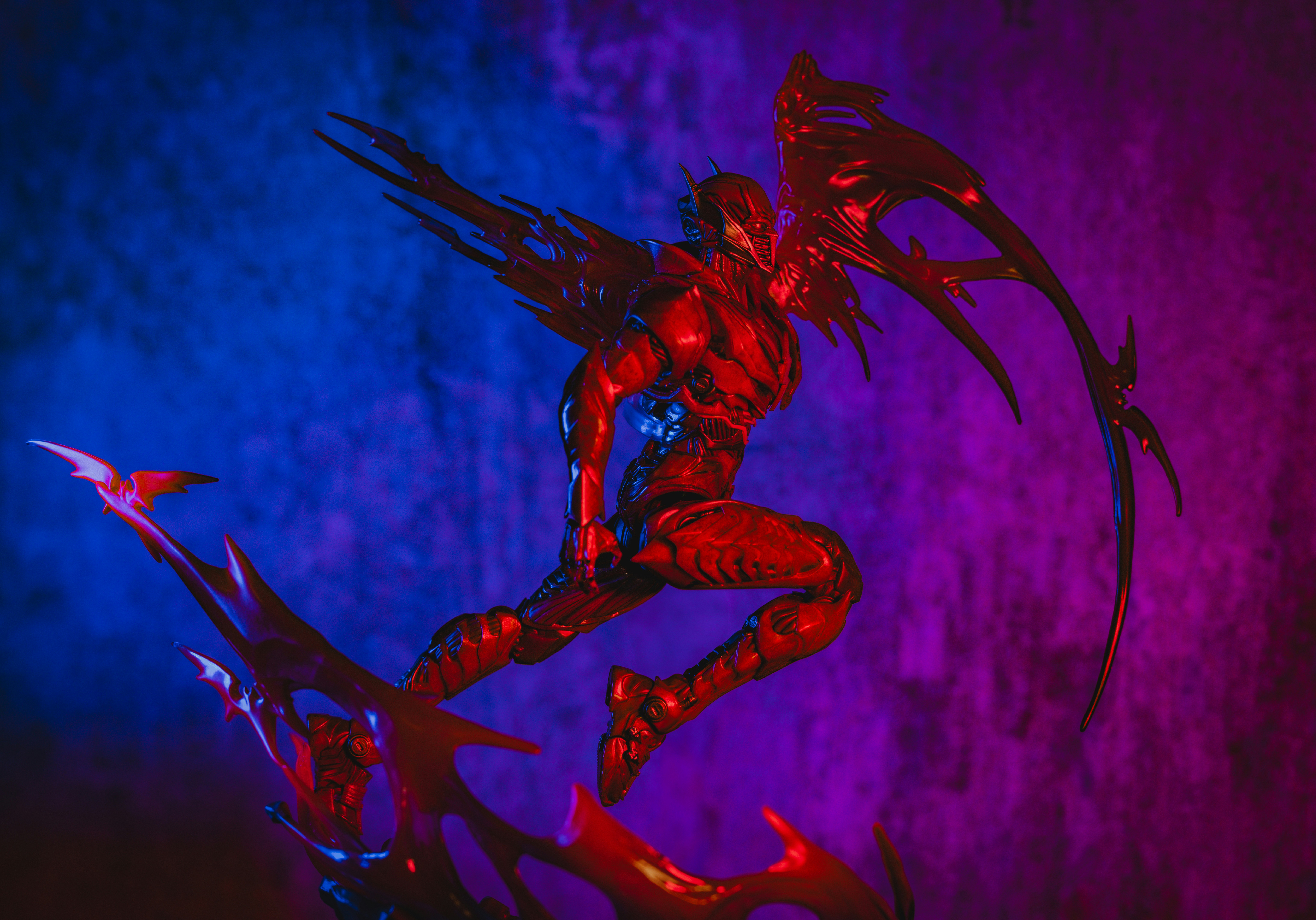 Uma figura de ação vermelha com armadura e asas saltando sobre um fundo azul e roxo