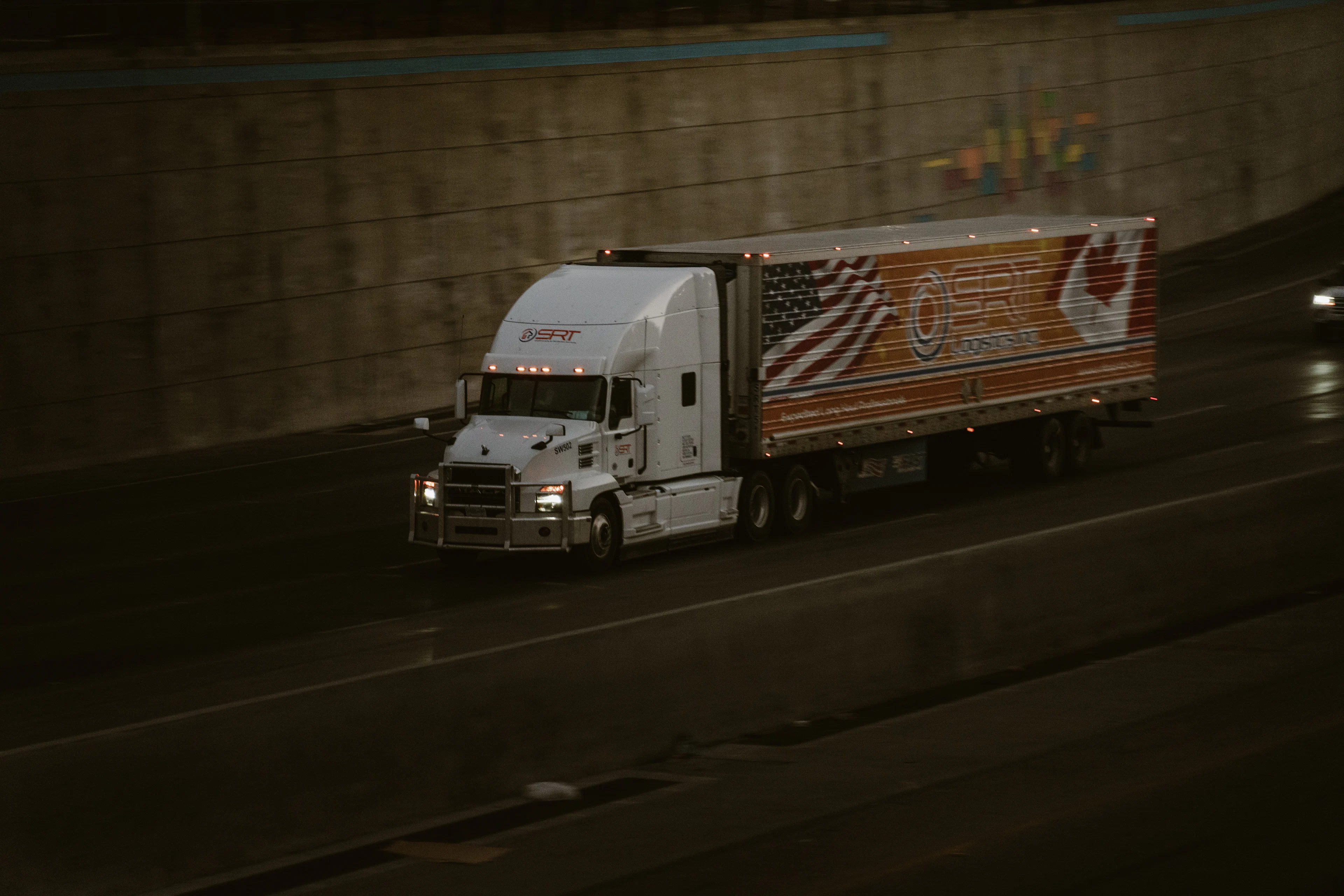 White semi-truck travelling on an interstate beside a concrete retaining wall