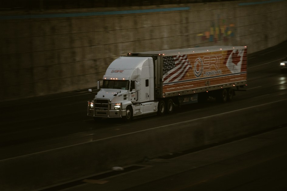 A white semi-truck driving along a highway beside a concrete retaining wall