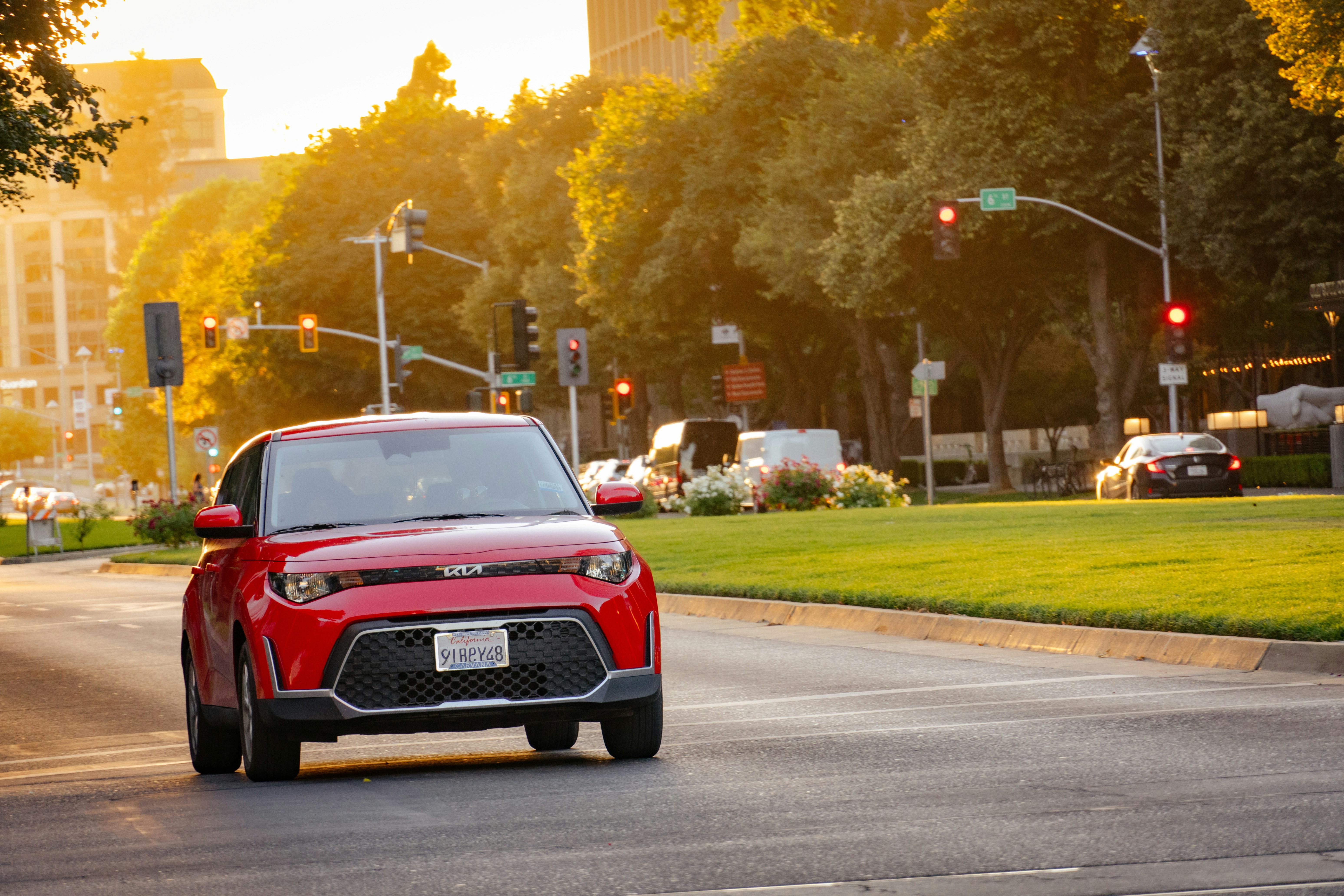 A red car driving on a city street during the golden hour