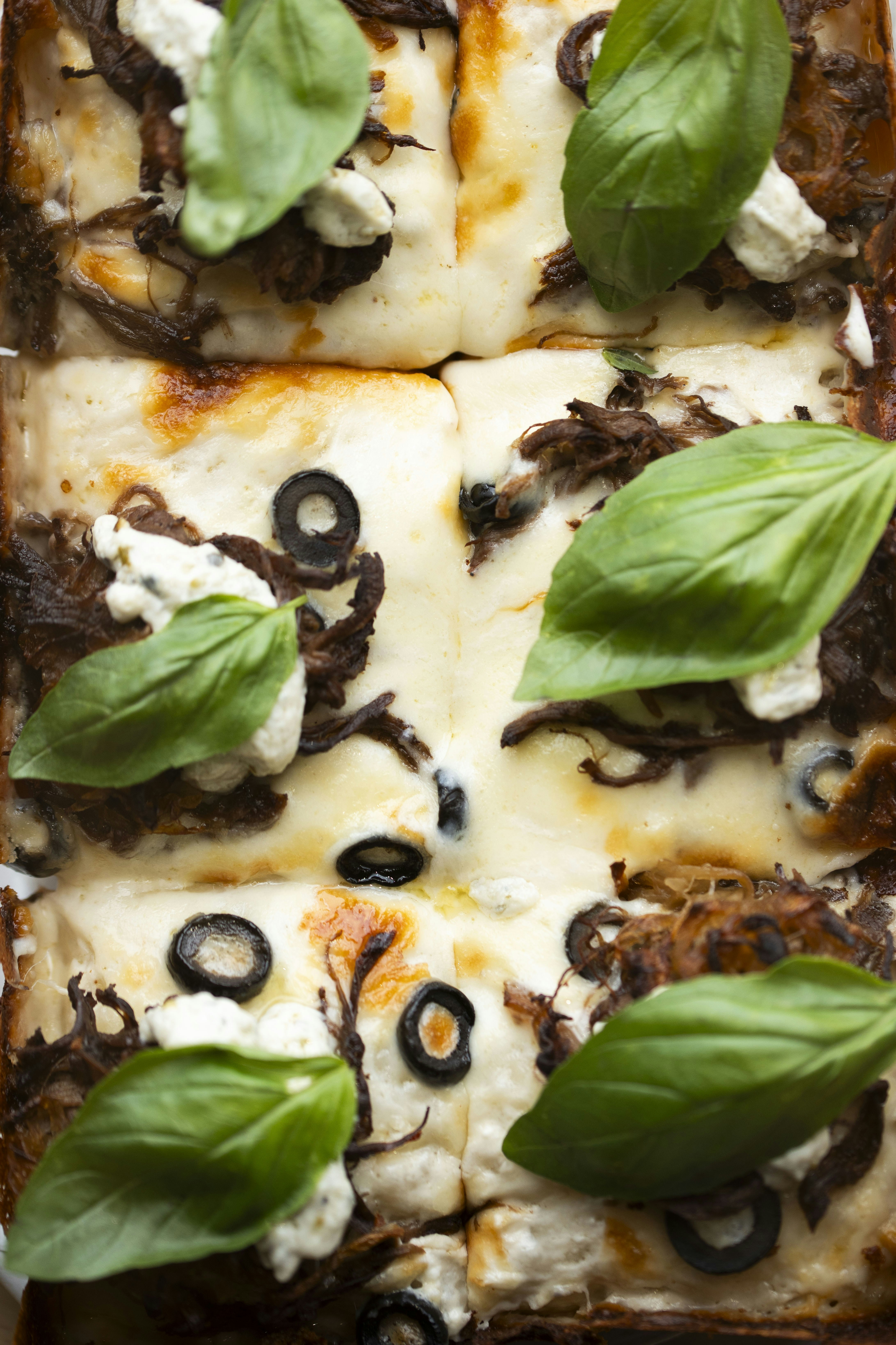 Foglio piatto al formaggio con carne grattugiata, olive nere e basilico fresco.
