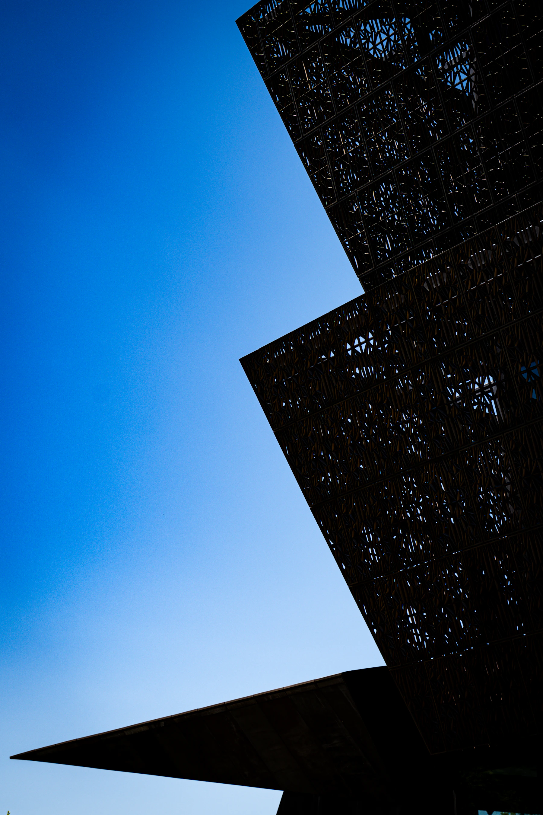 Angled bronze-colored lattice façade of the National Museum of African American History and Culture against a blue sky.