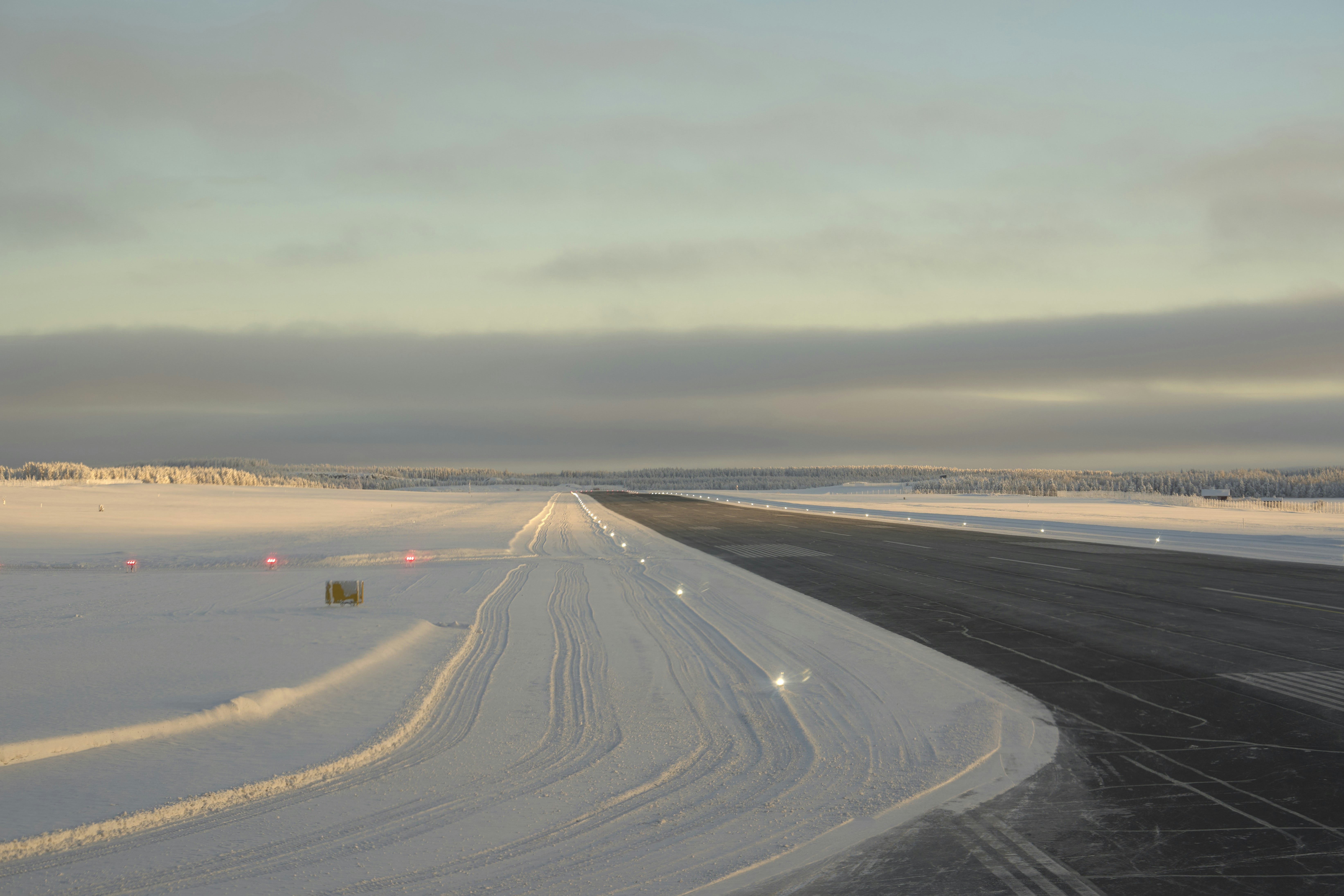 Snow-covered airport runway with lights under a cloudy sky.