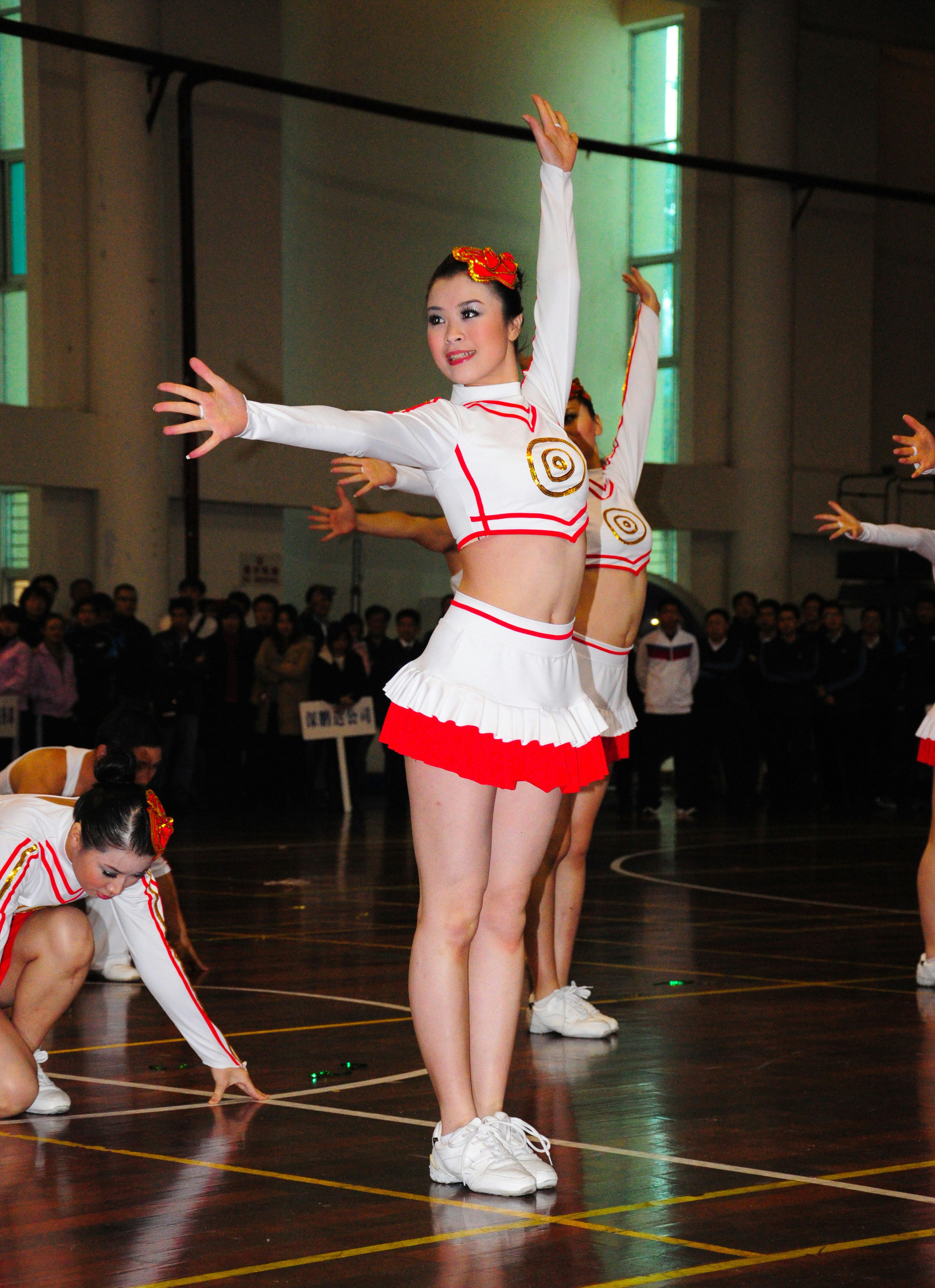 A group of cheerleaders in white and red uniforms performing on a wooden court