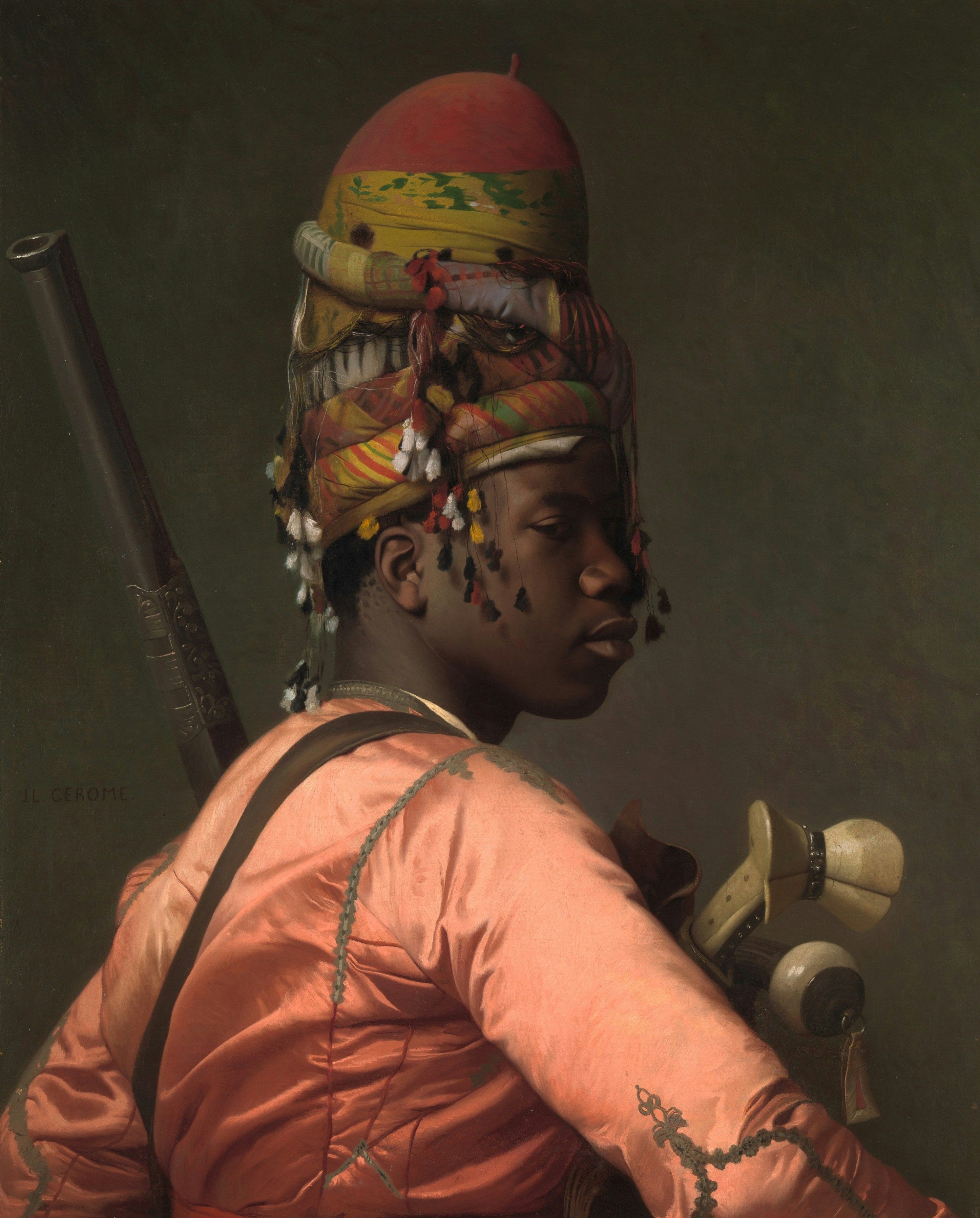 A person wearing a tall, colorful turban and a peach-colored tunic with a rifle.