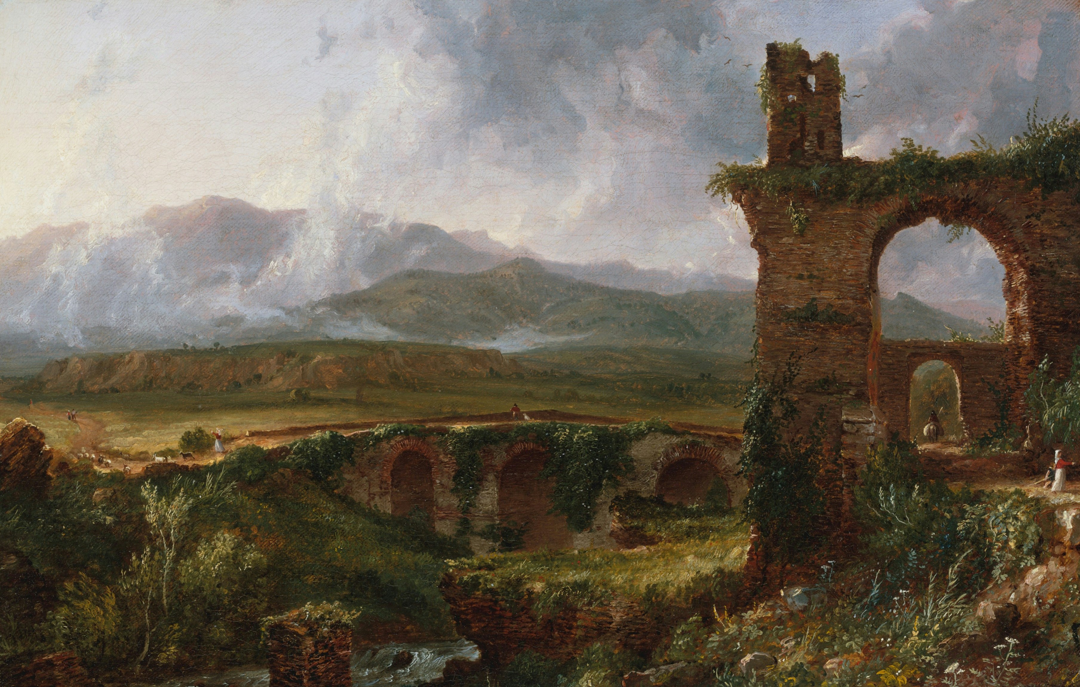 Ancient brick ruins with arches overlooking a green valley and distant mountains.