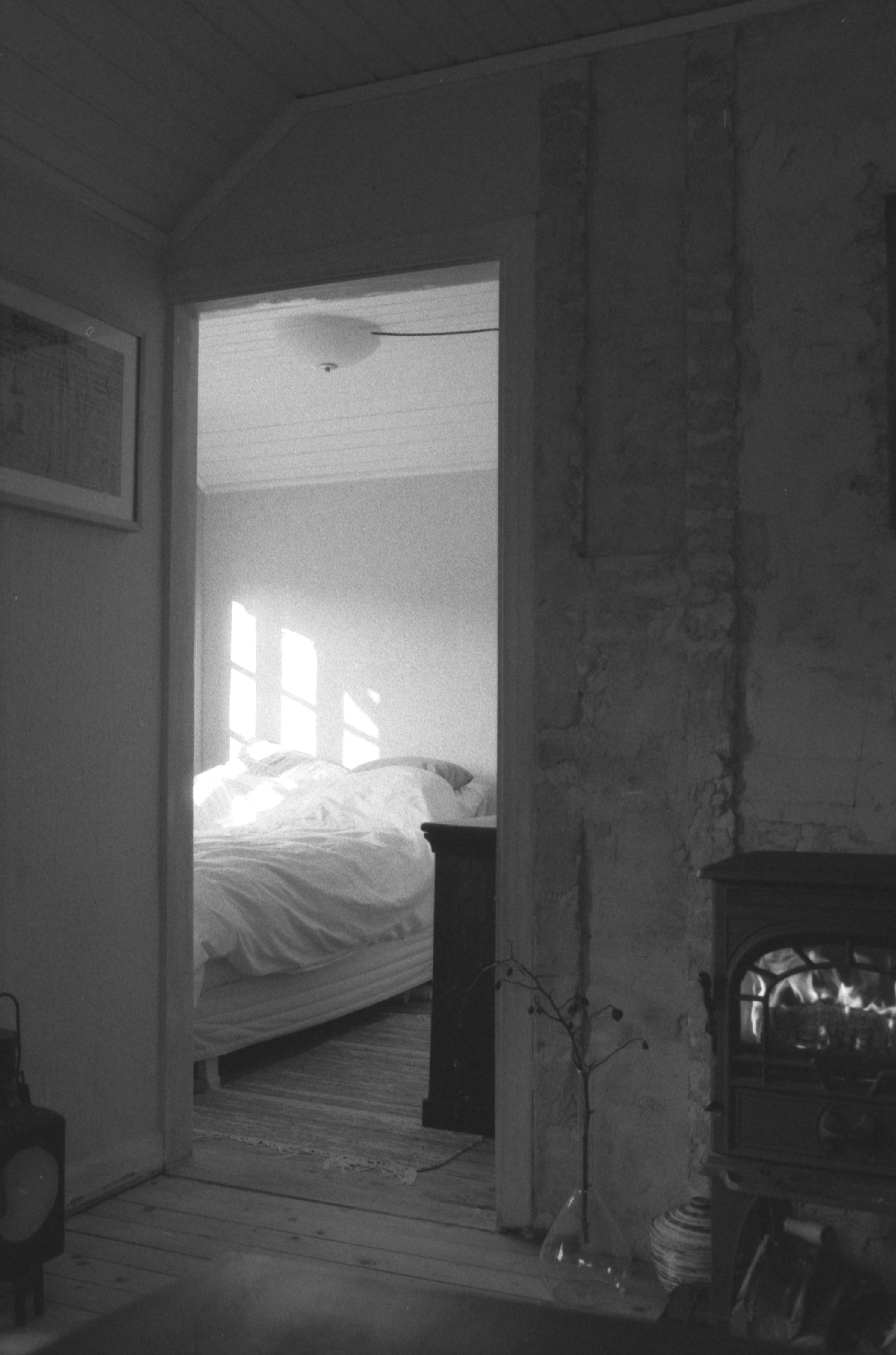 A view through a doorway into a sunlit bedroom with a made bed