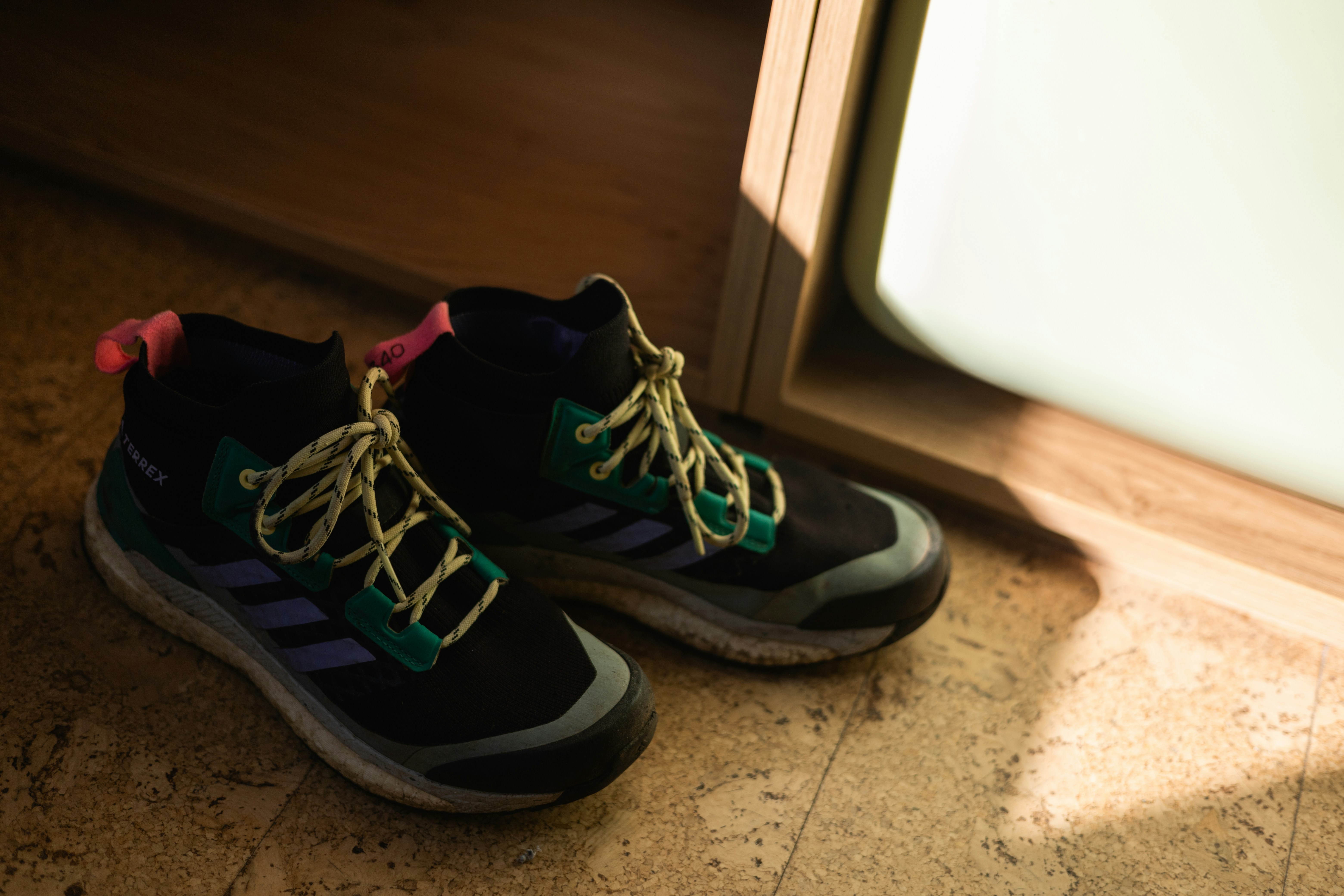 Dos botas negras de senderismo con cordones amarillos sobre un suelo texturizado bajo el sol
