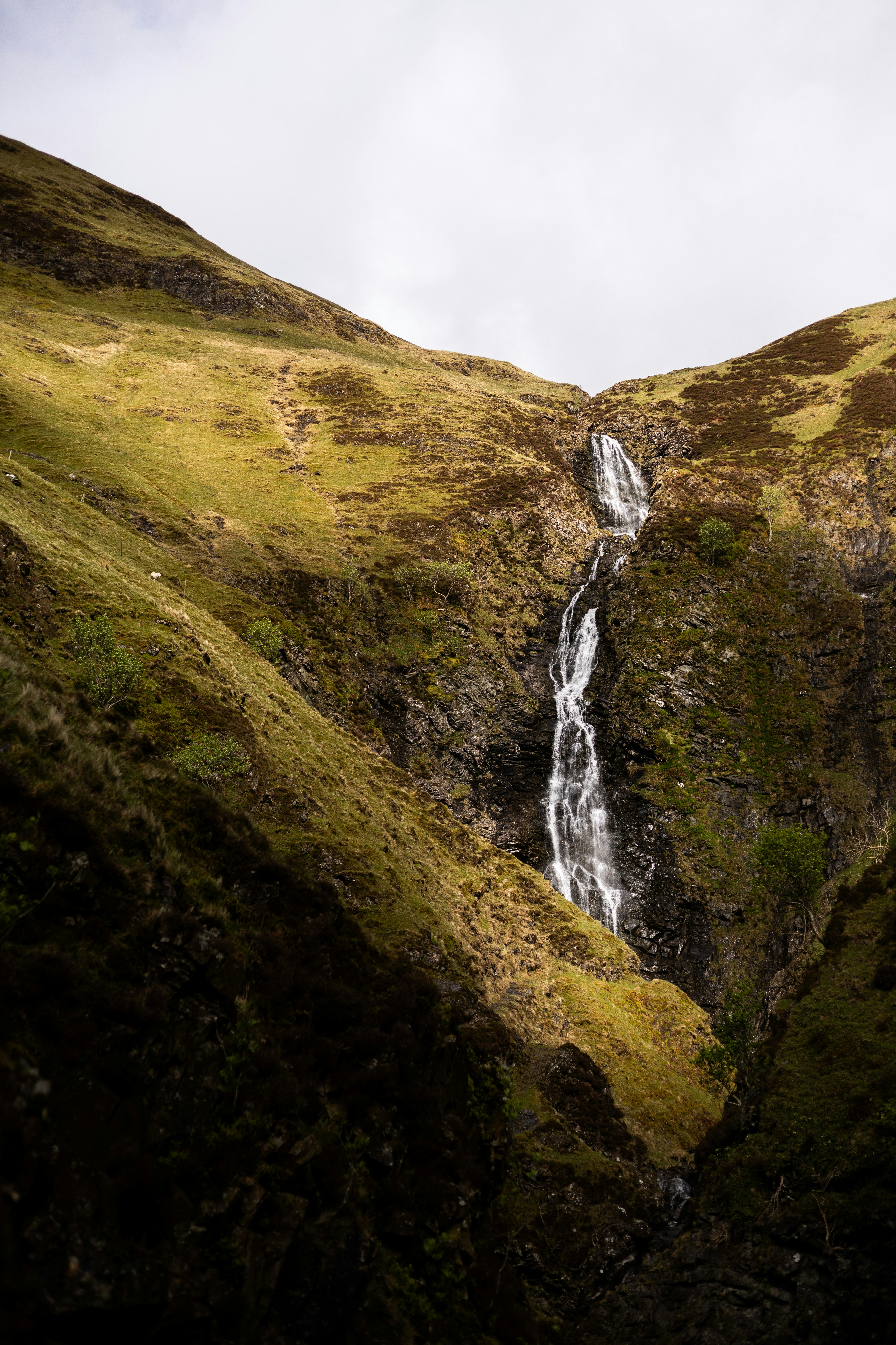 Una alta cascada que cae por una empinada ladera cubierta de hierba en la montaña