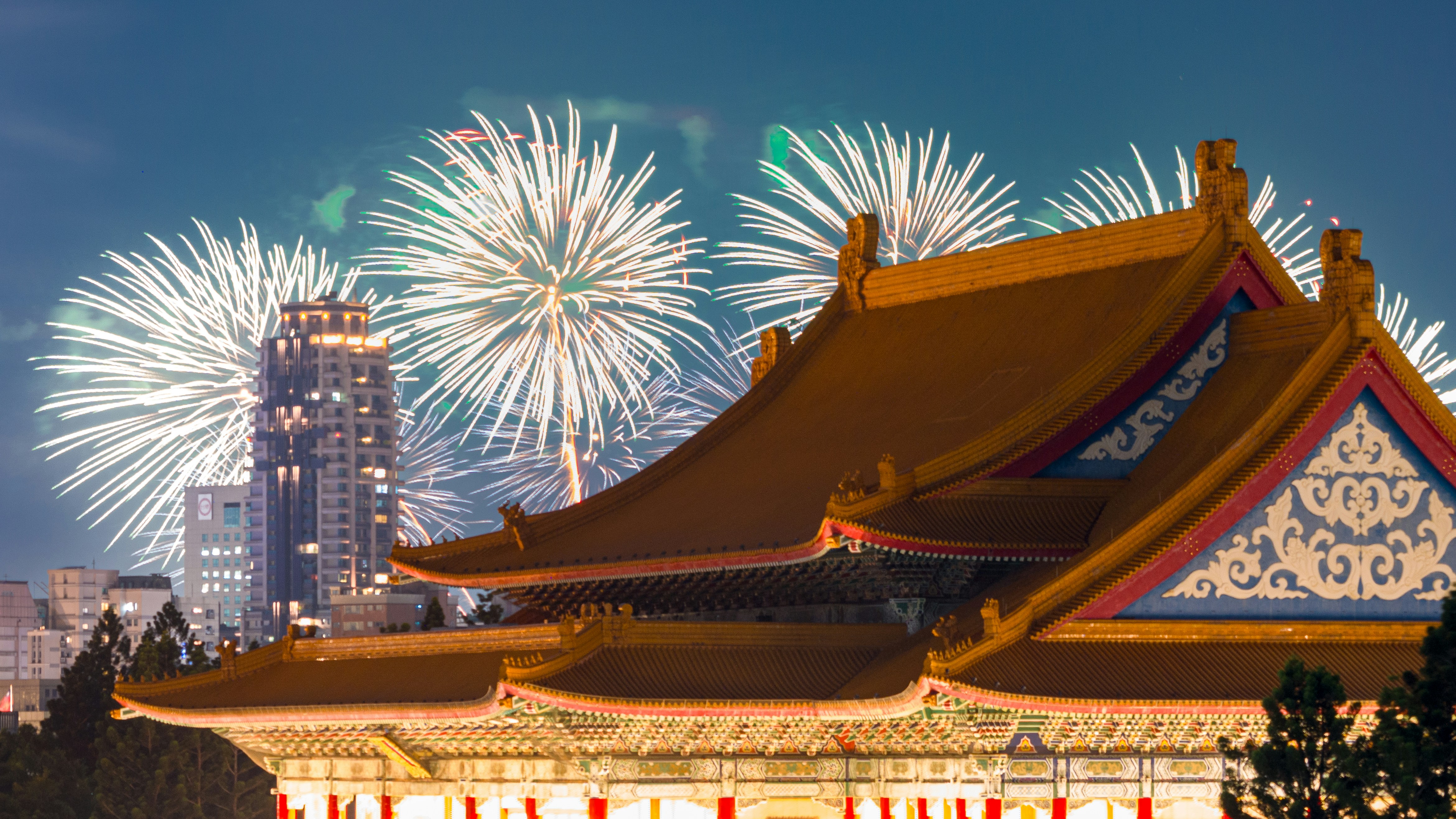 White fireworks exploding over a traditional Chinese temple roof in Taipei at night.