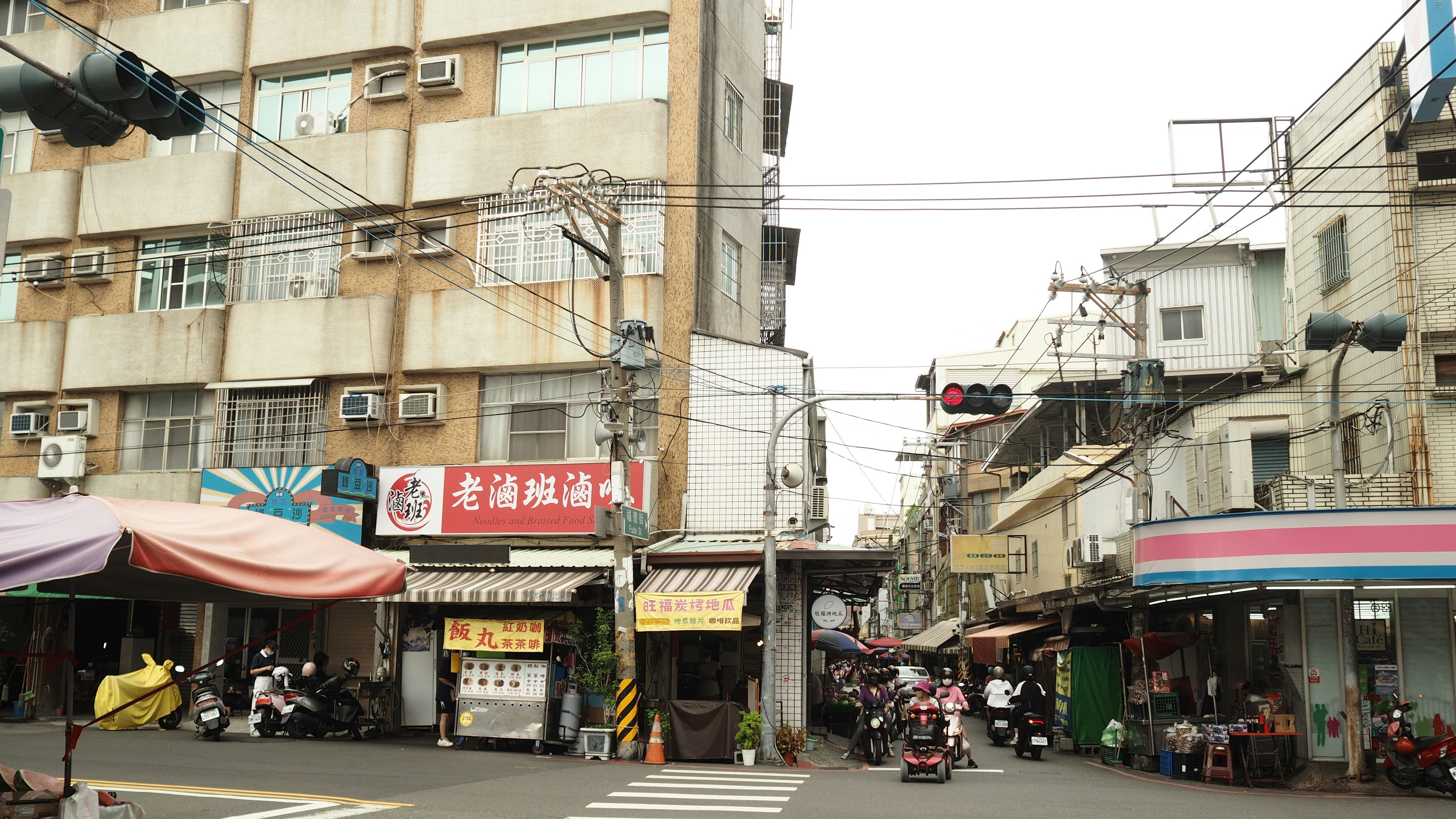 台湾の交通量の多い交差点で、バイクや店舗、架空の電線が並んでいます