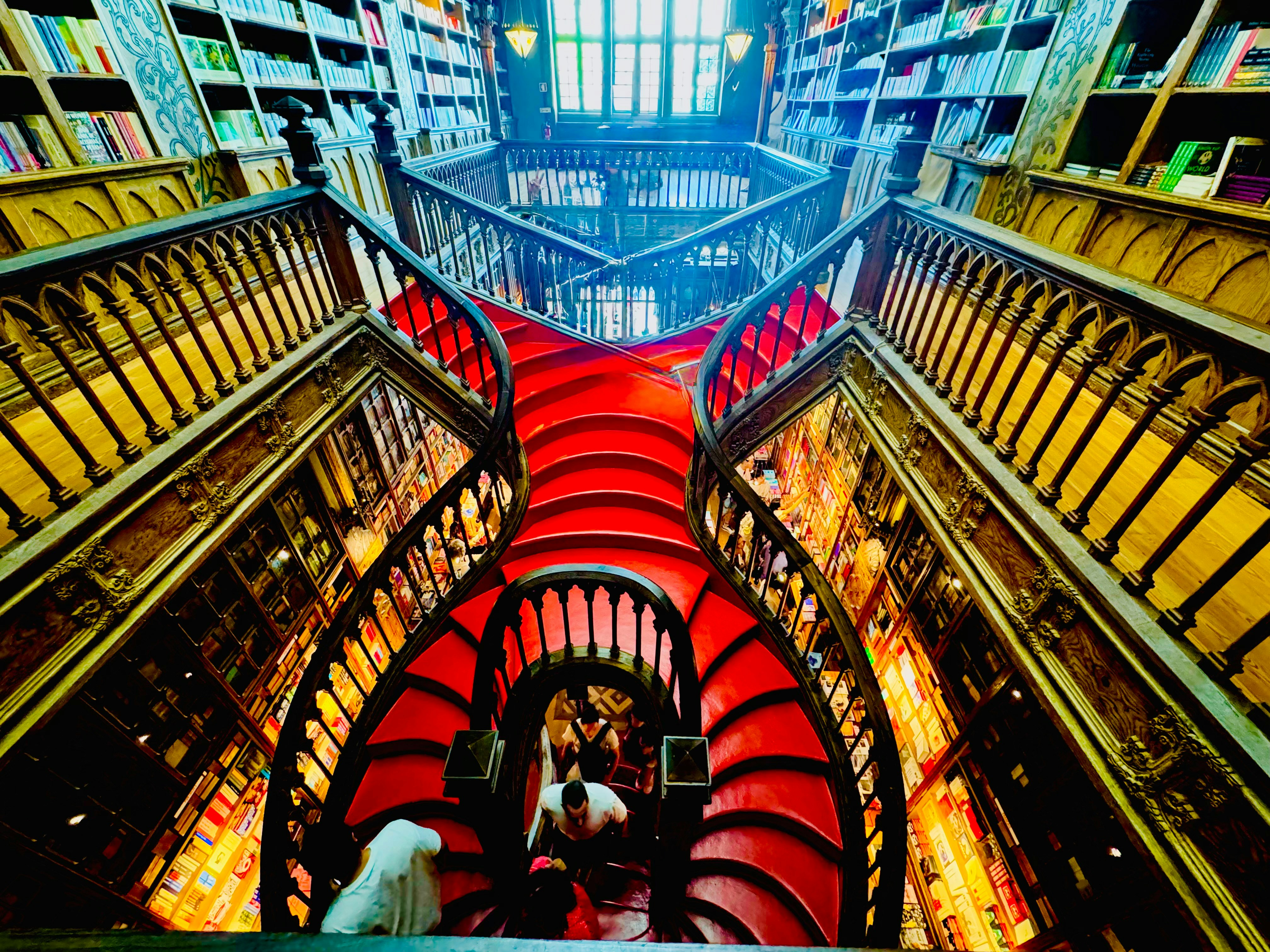 A bright red curved staircase in a multi-level library with wooden bookshelves.