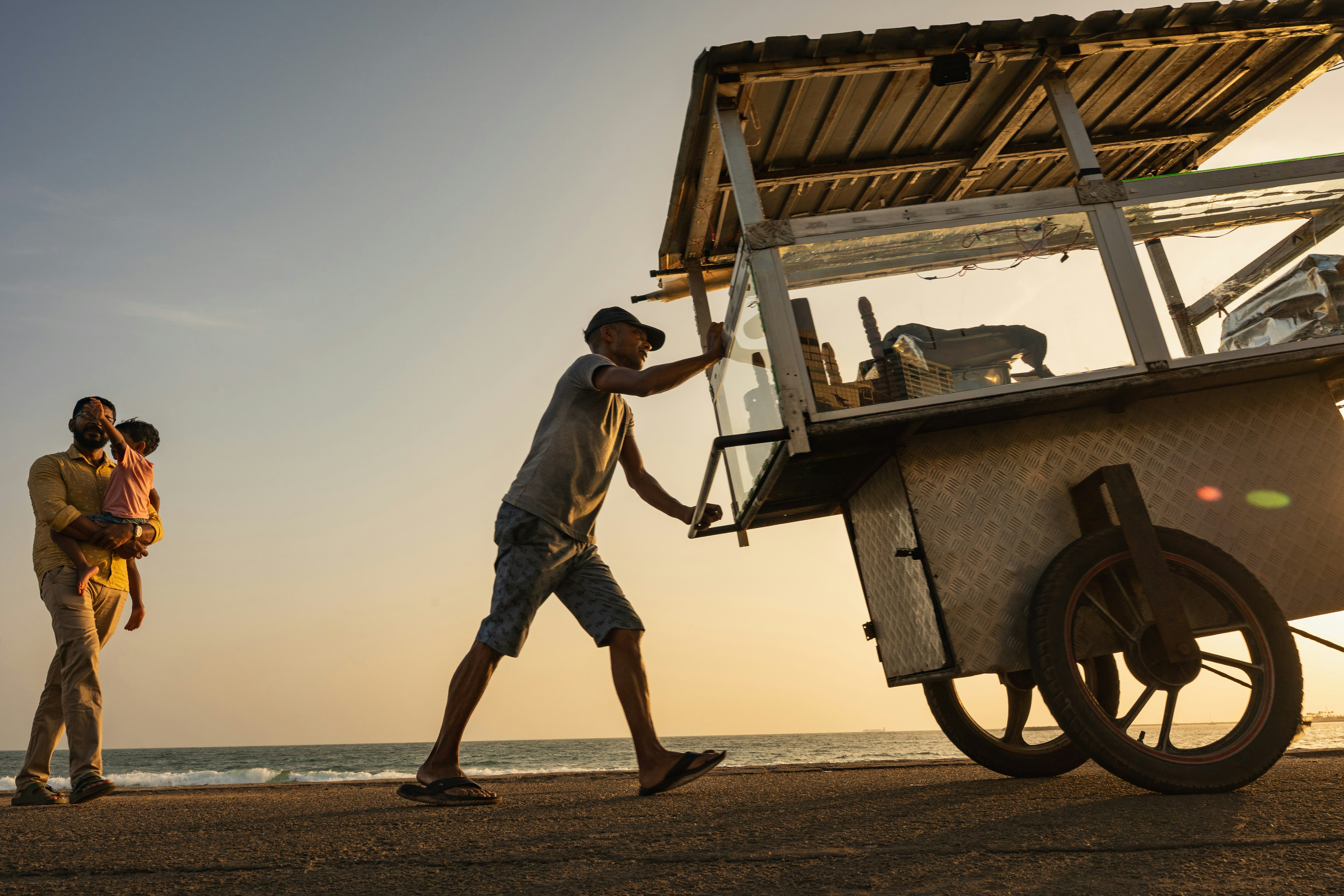 A person pushing a food cart along a beach at low sun