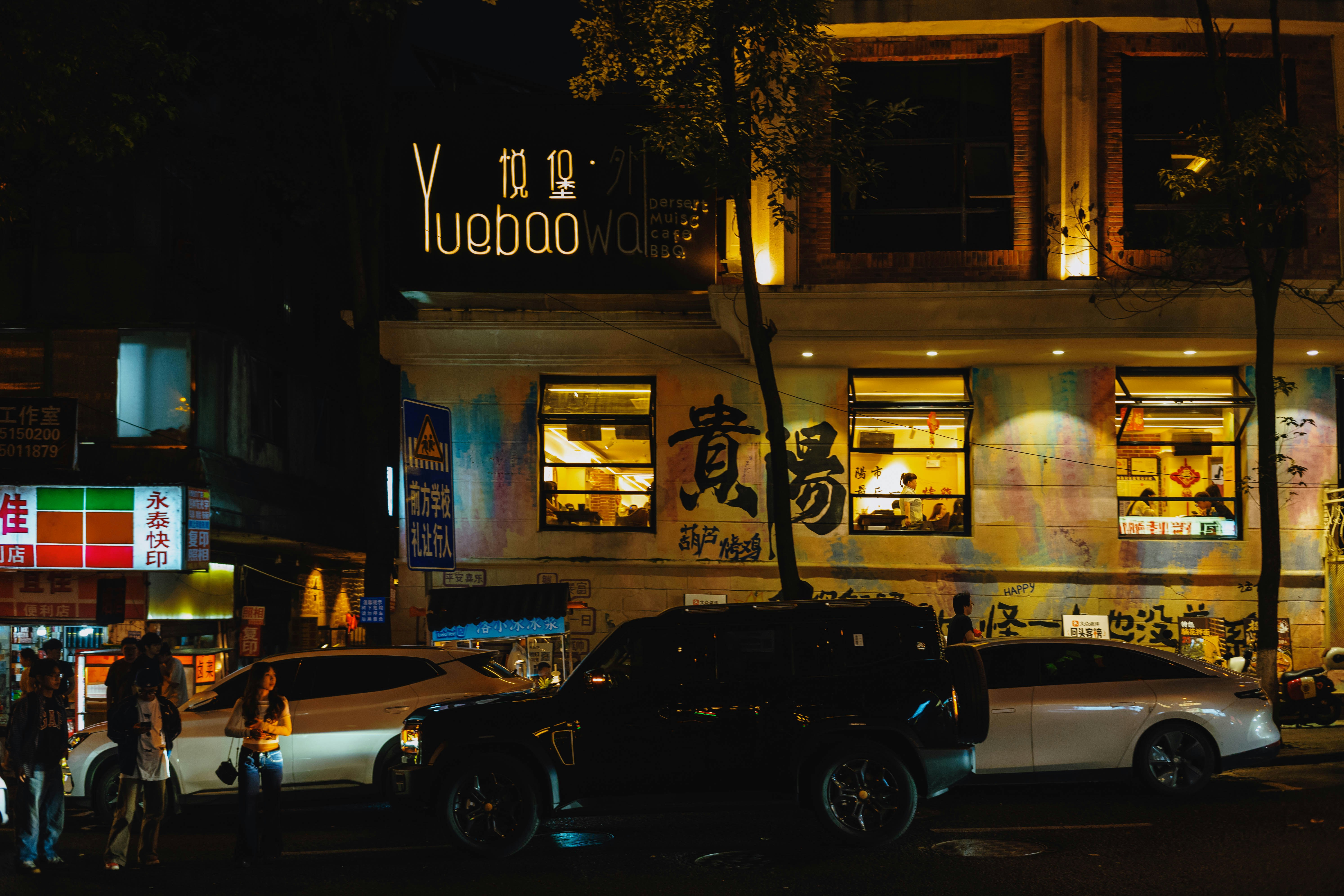 A black SUV parked on a city street at night in front of a restaurant
